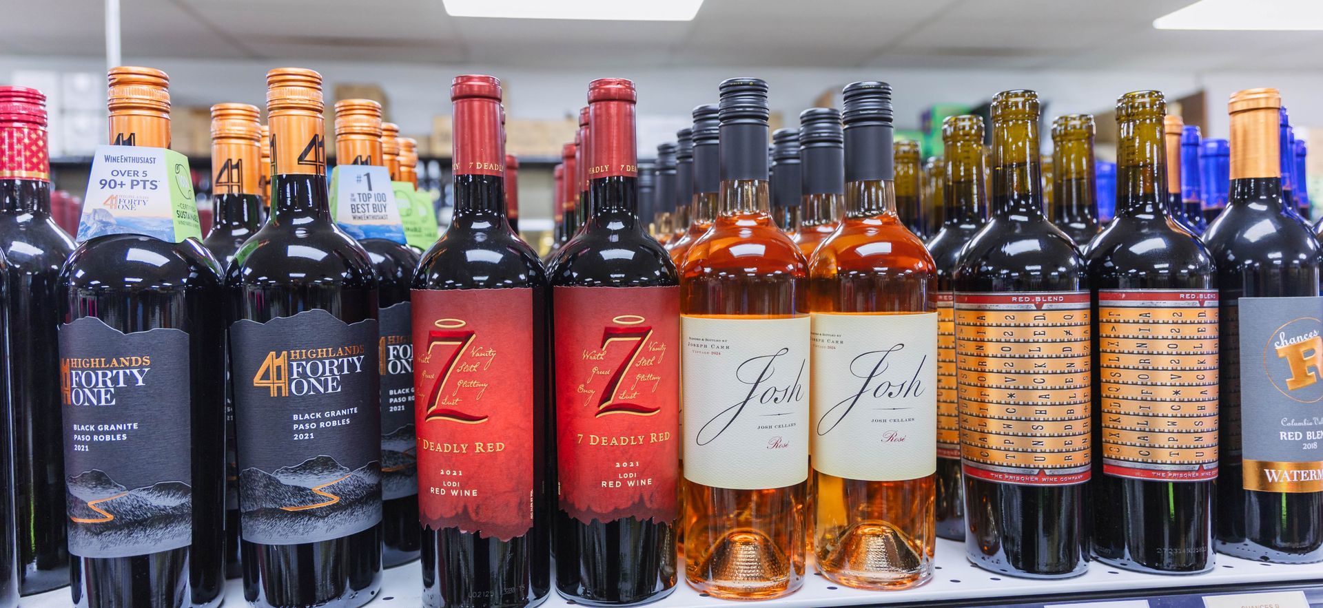 Bottles of wine on a store shelf, various brands and colors, some with tags.