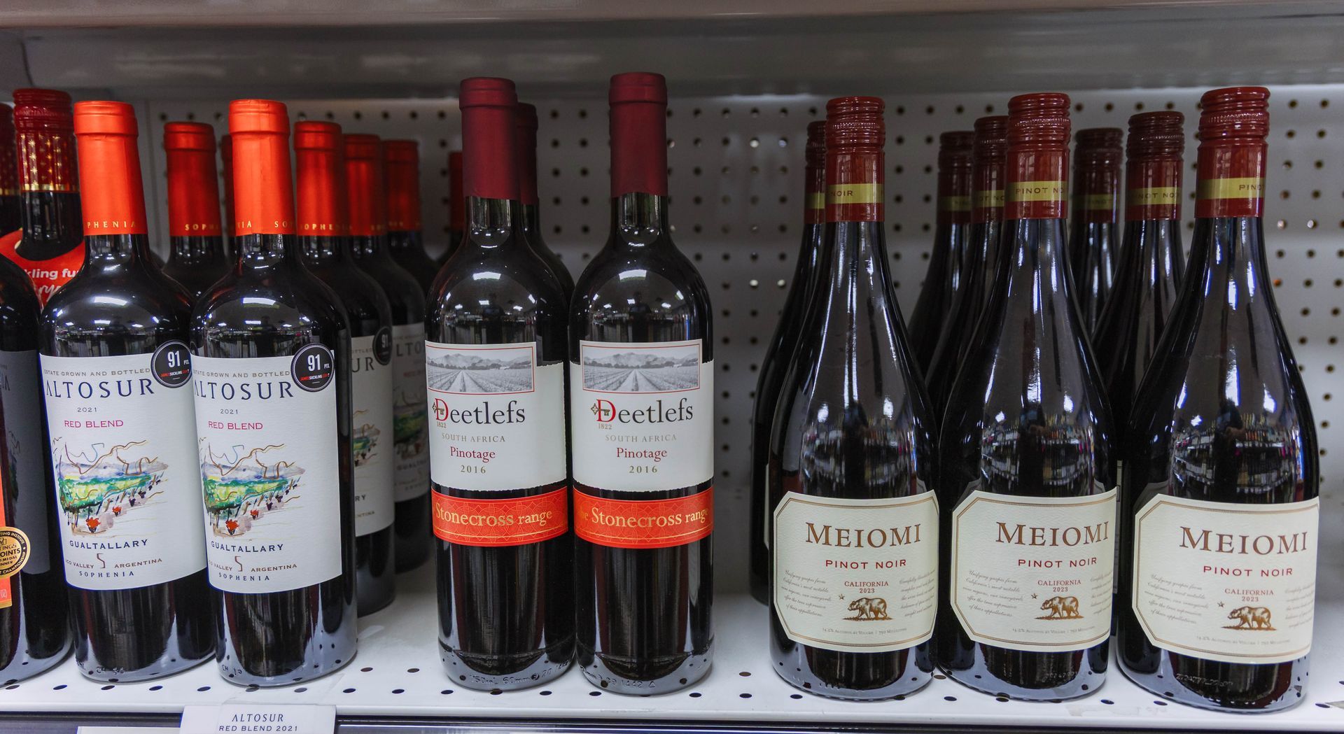 Shelves stocked with various red wine bottles, with labels and orange seals.