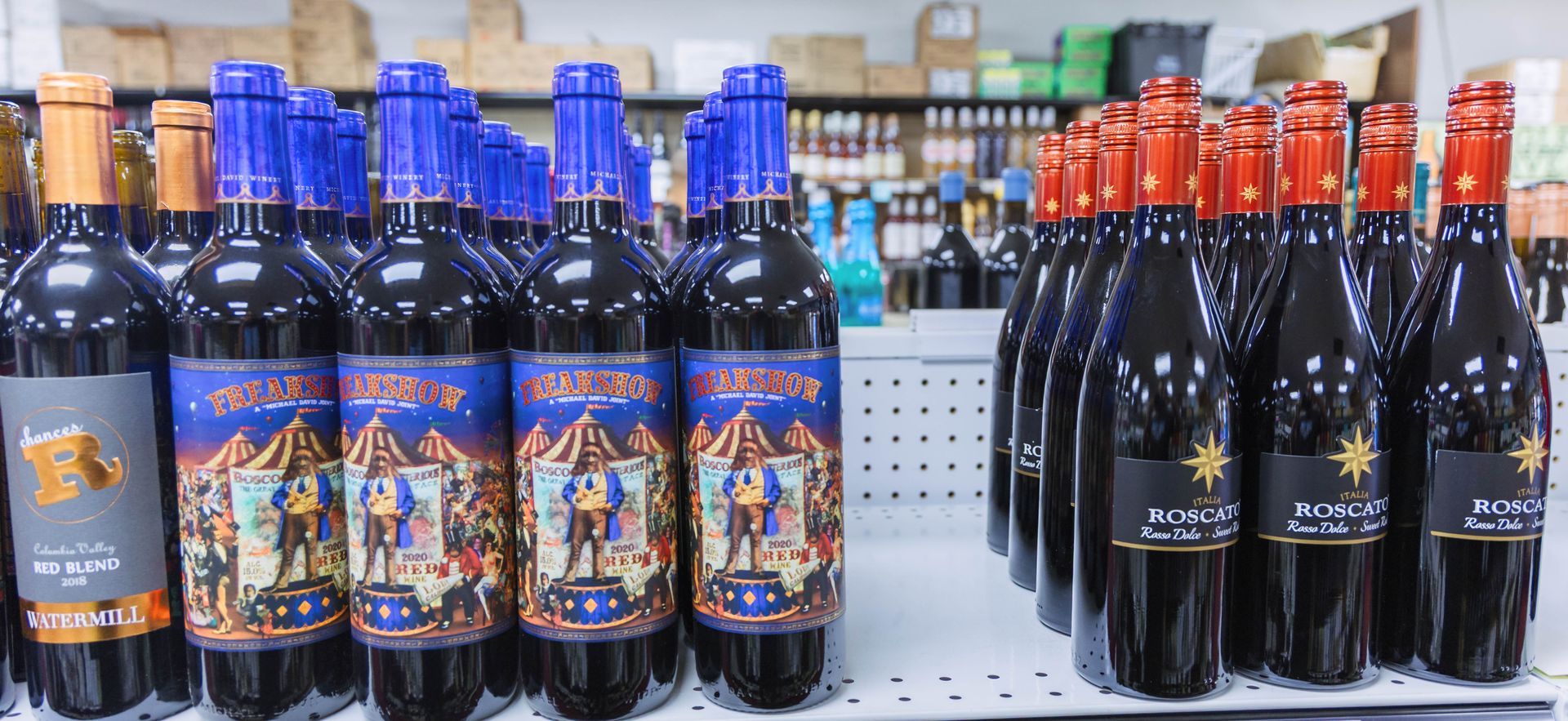 Wine bottles on a shelf with labels featuring circus and star designs, in a store setting.