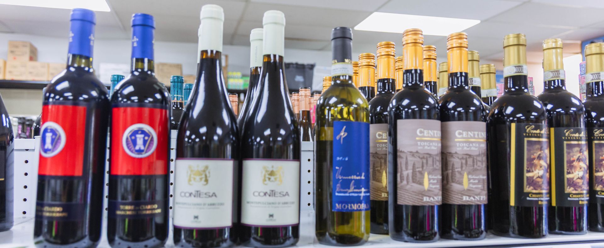 Bottles of wine on a shelf; a shop interior. Dark glass bottles with colorful labels and foil.
