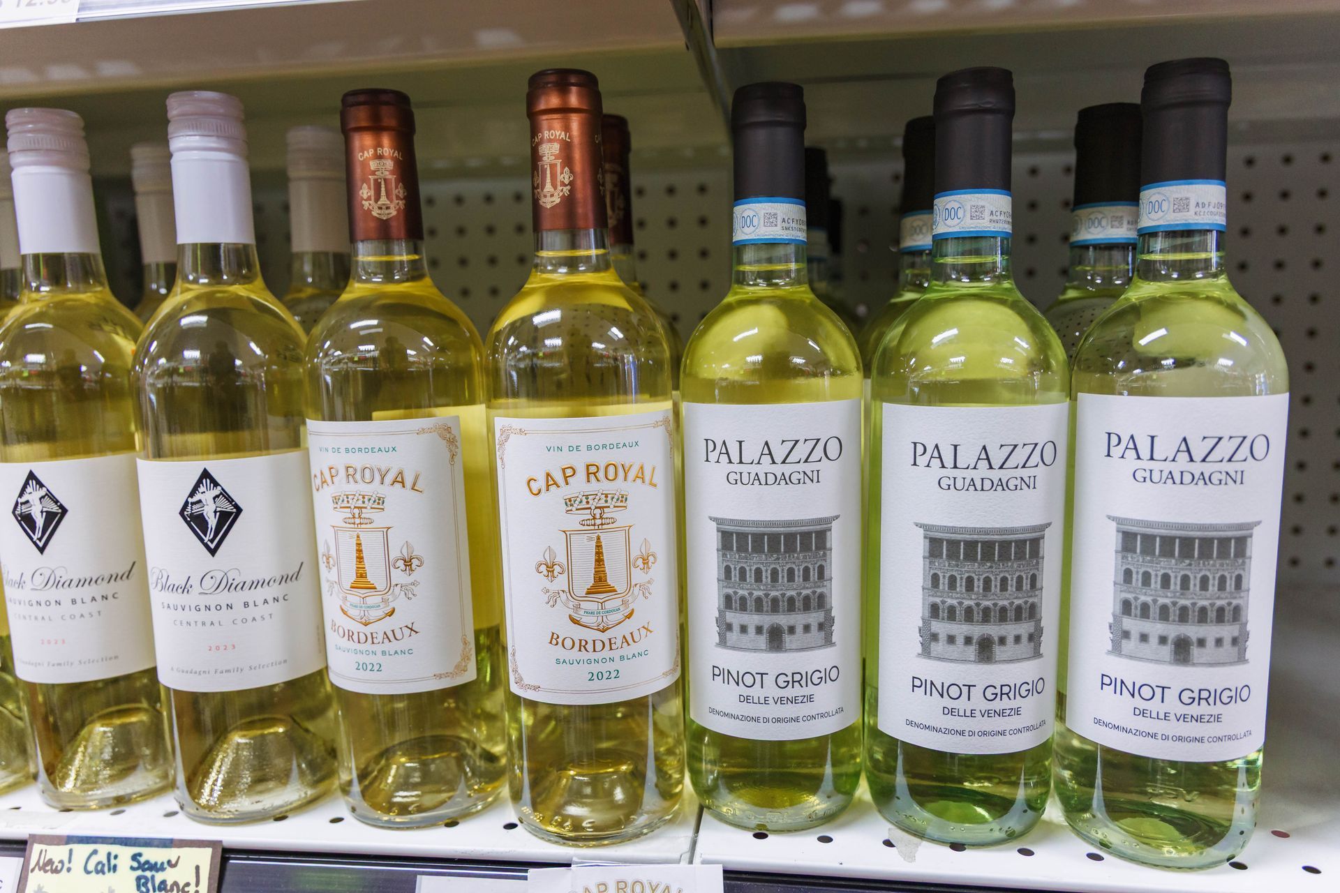 Wine bottles on a shelf, mostly yellow and green liquid, different labels.