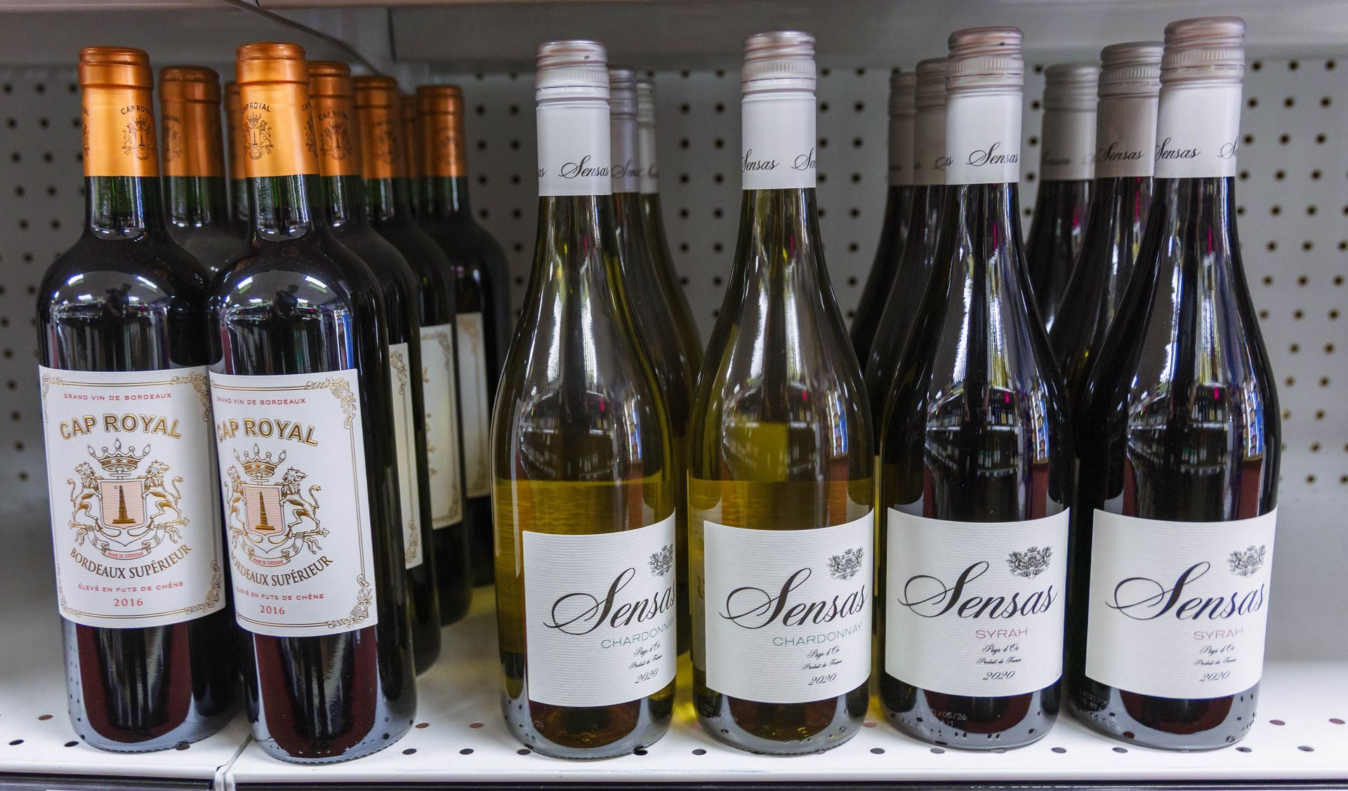Bottles of red and white wine on a store shelf, labeled with gold and white details.