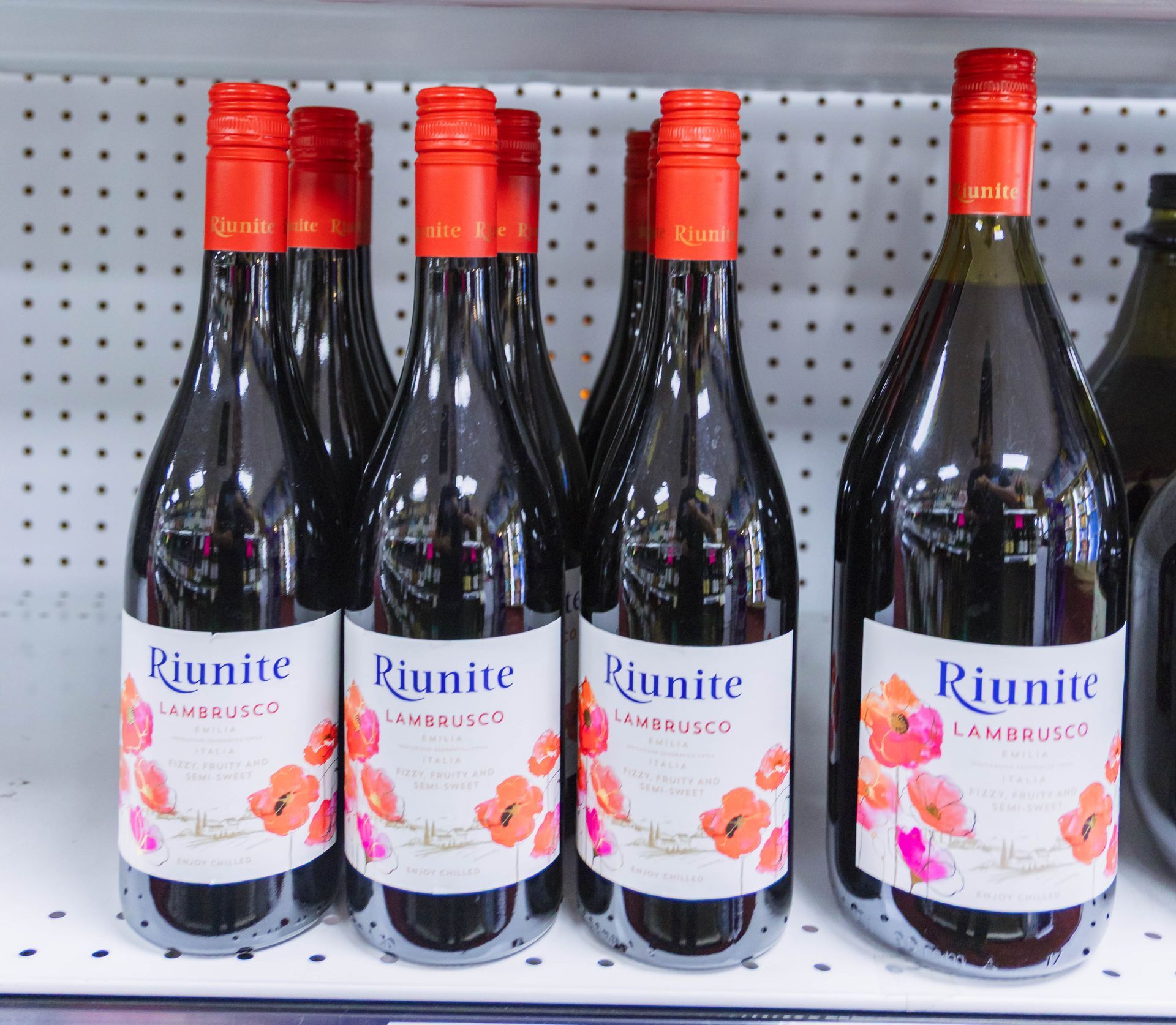 Bottles of Riunite Lambrusco wine on a shelf, red caps and labels with floral design.