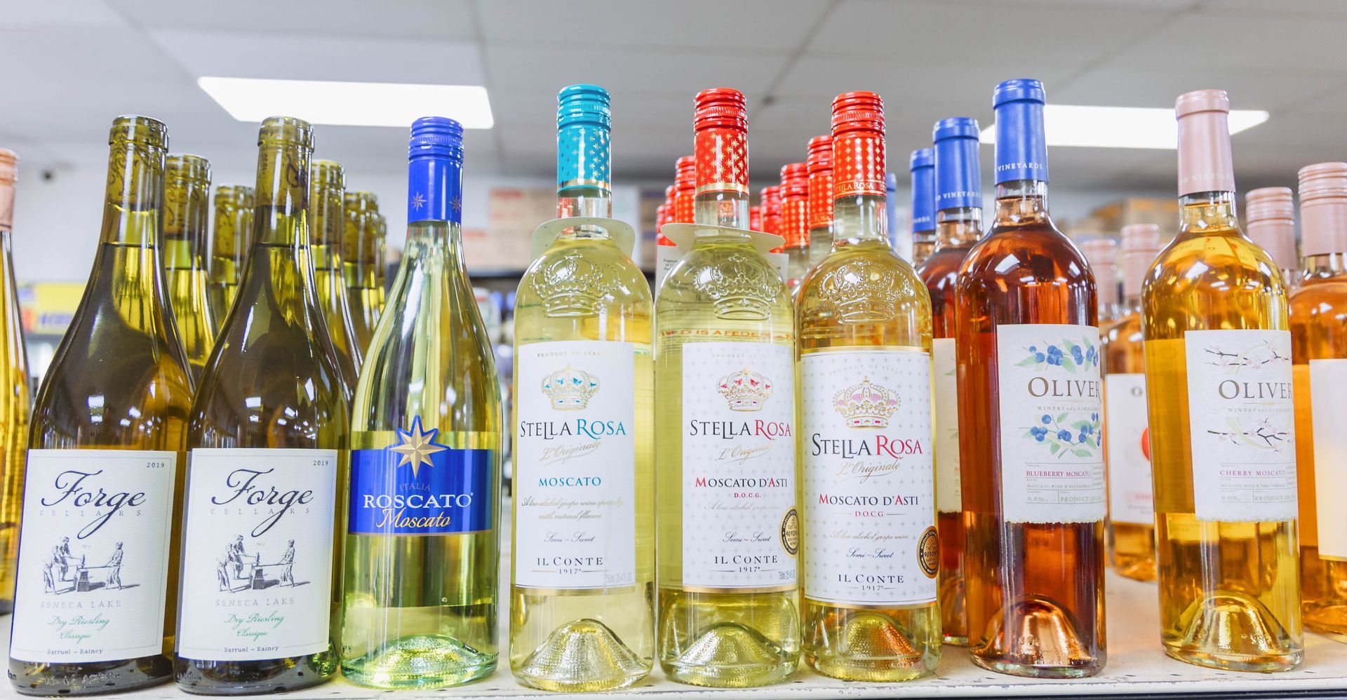 Bottles of wine on a shelf. Various colors of wine and bottle caps. Store setting.