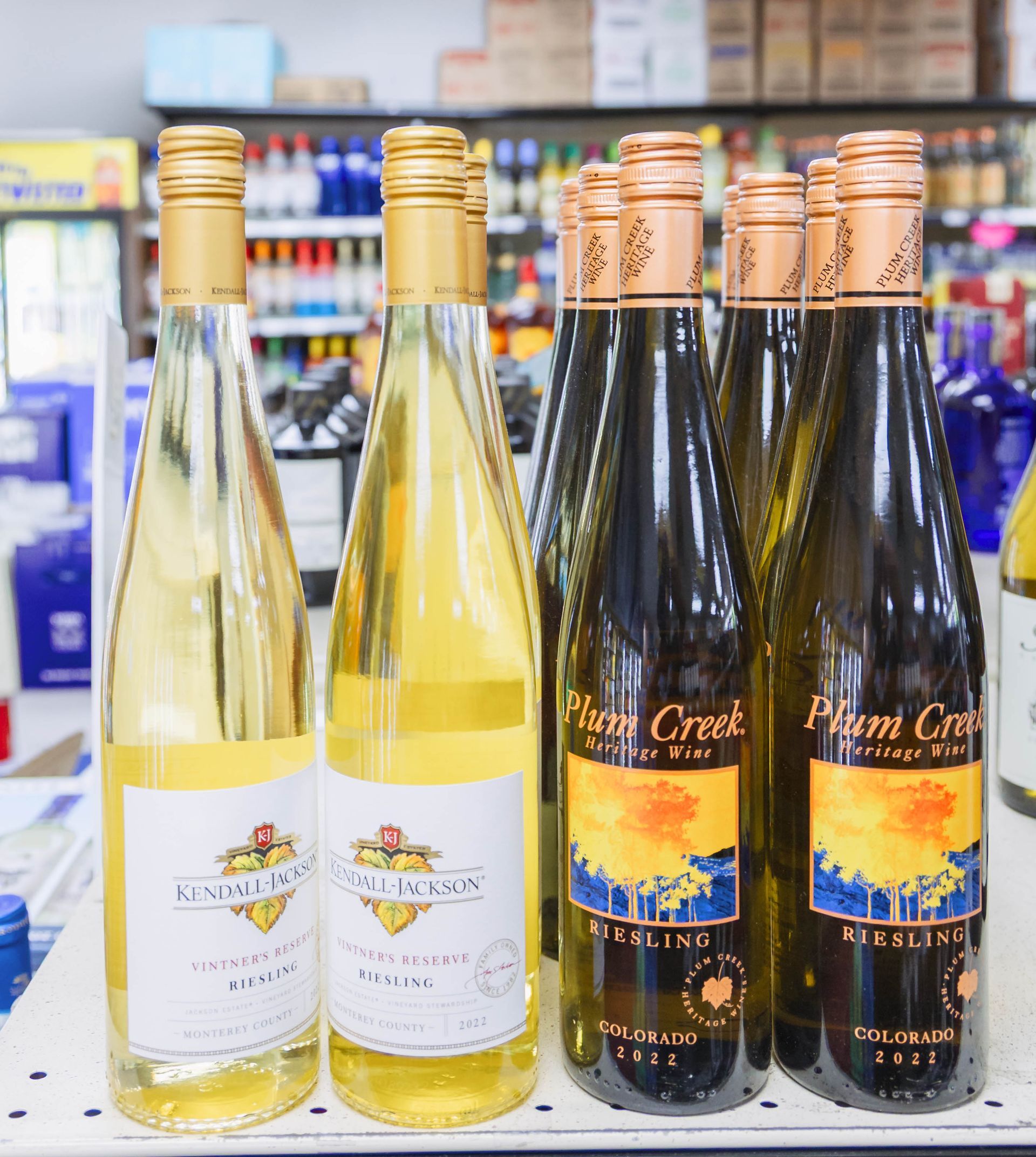 Bottles of white wine on a shelf in a store, with golden caps and colorful labels.