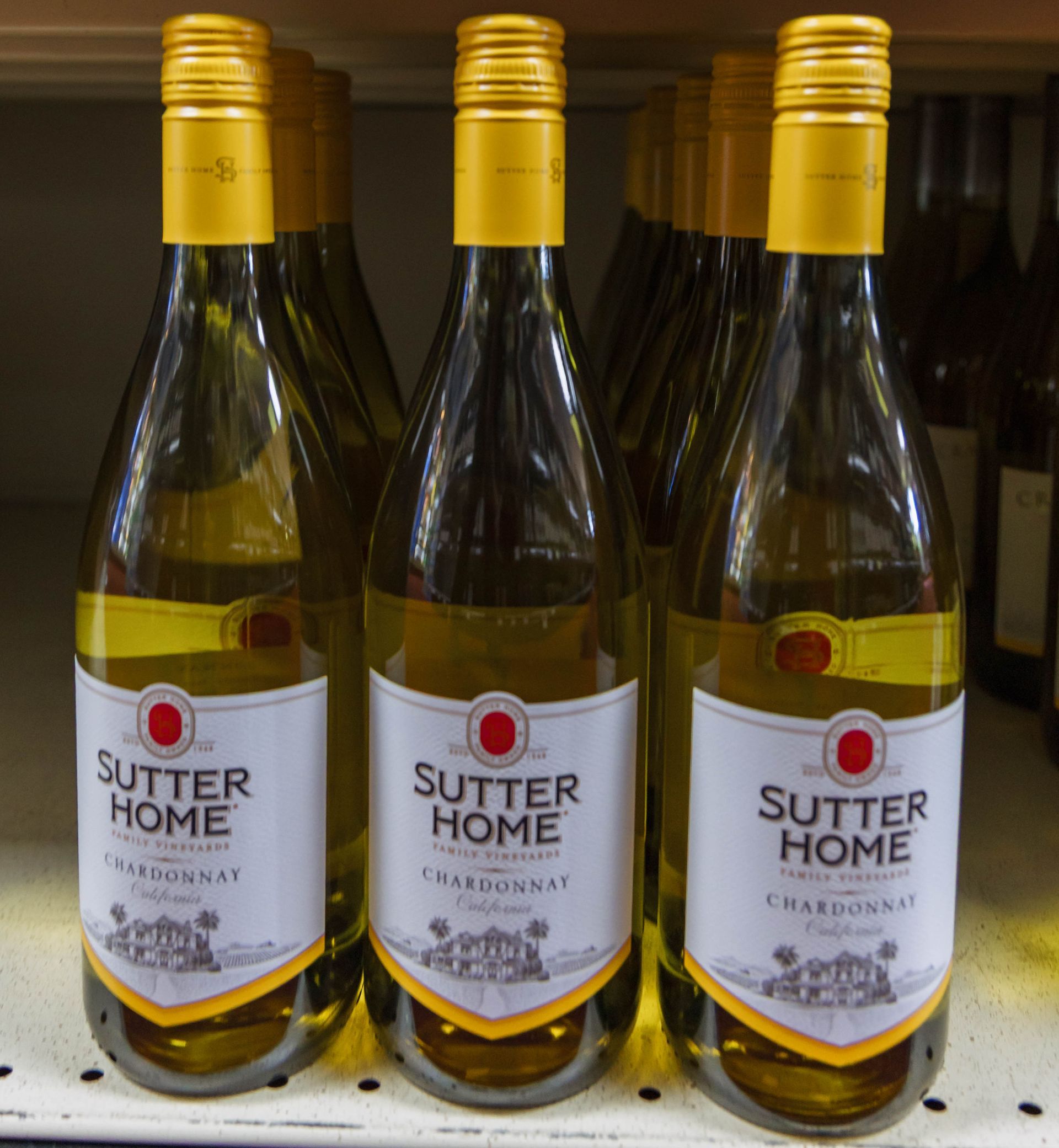 Bottles of Sutter Home Chardonnay wine with yellow caps and labels, on a shelf.
