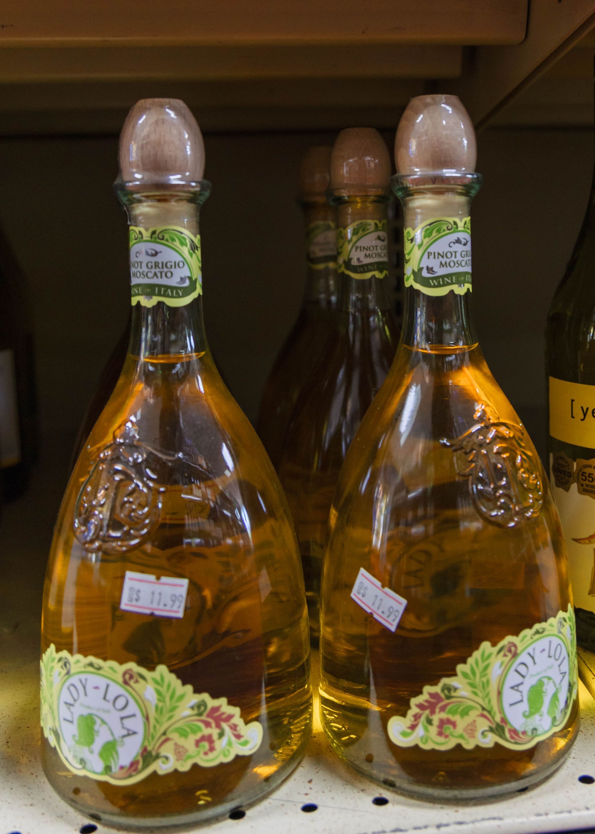 Bottles of Lady Lola liqueur on a shelf. Tall, clear bottles with brown liquor and green labels.