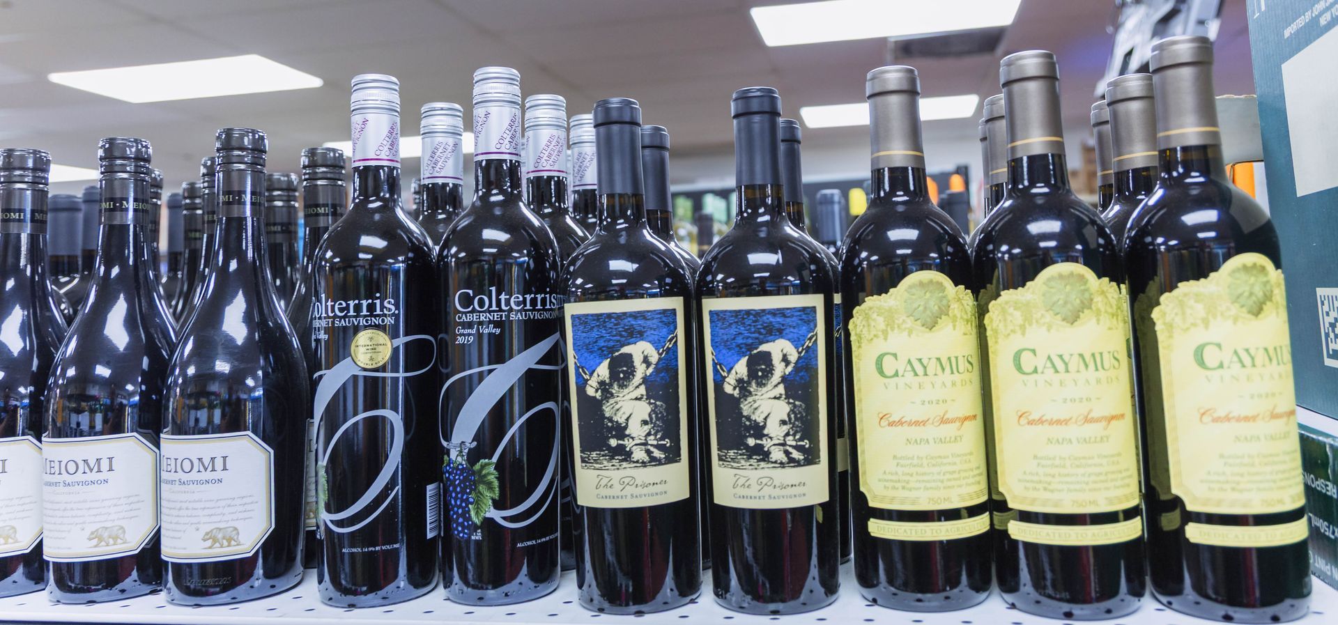 Wine bottles on a store shelf; dark glass, various labels with black, blue, and yellow backgrounds.