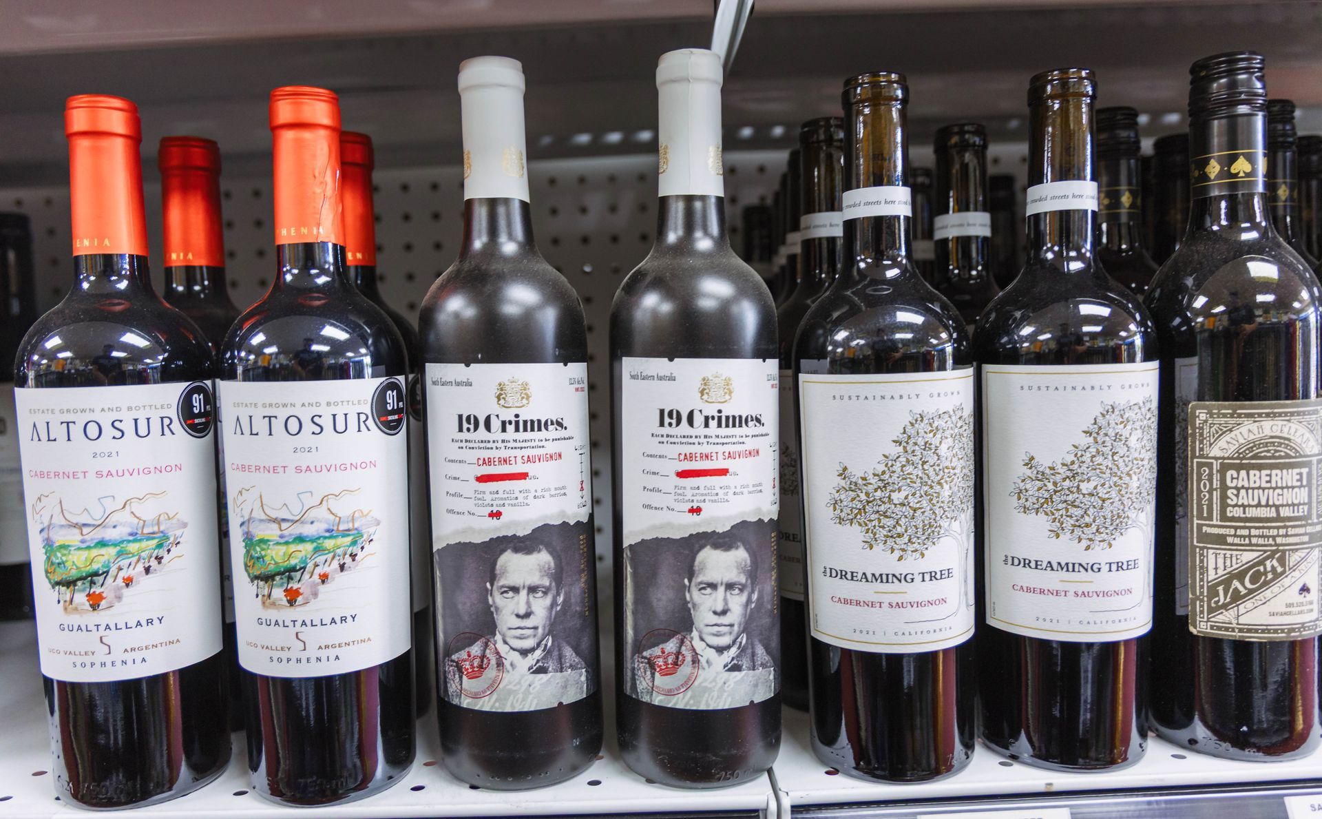 Rows of wine bottles on a store shelf. Labels vary, primarily red wine.