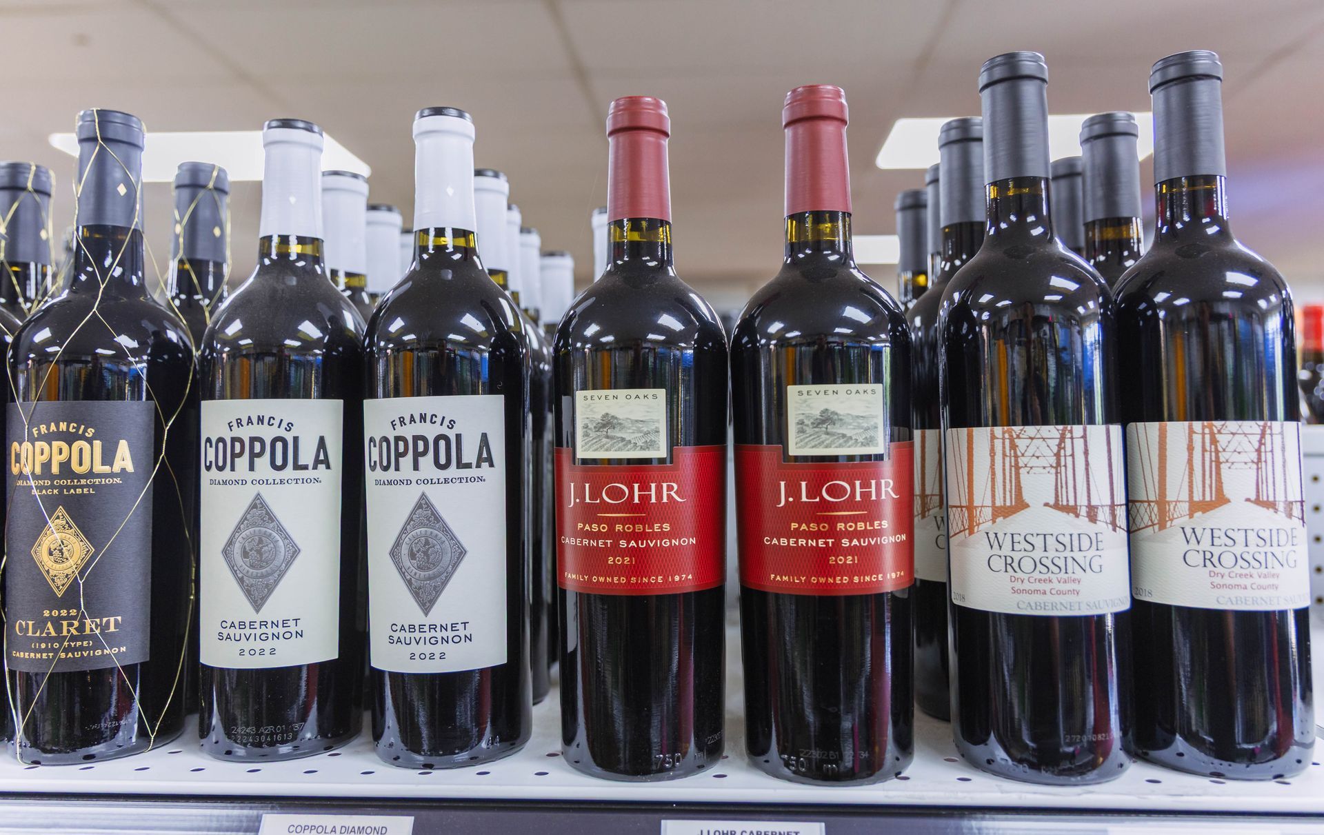 Wine bottles on a shelf. Various brands with red and white labels. Dark red wine.