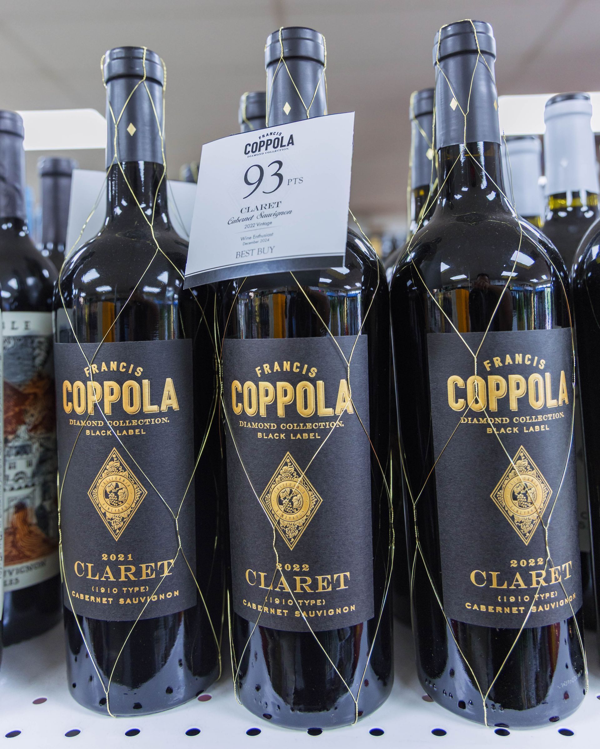 Rows of Francis Ford Coppola Claret wine bottles on a store shelf, black labels with gold details, price tag.