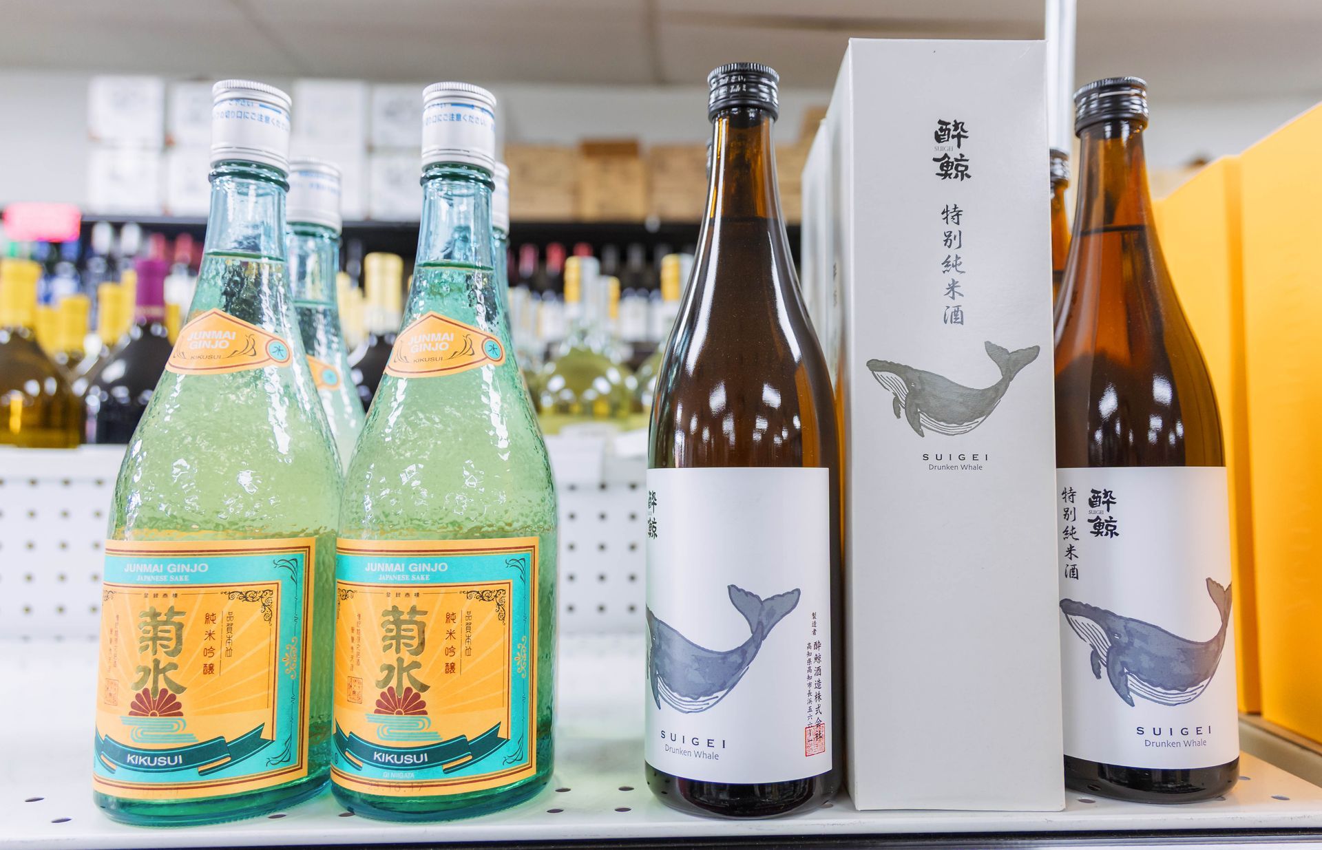 Bottles of Japanese sake with colorful labels and a whale motif on a shelf in a store.