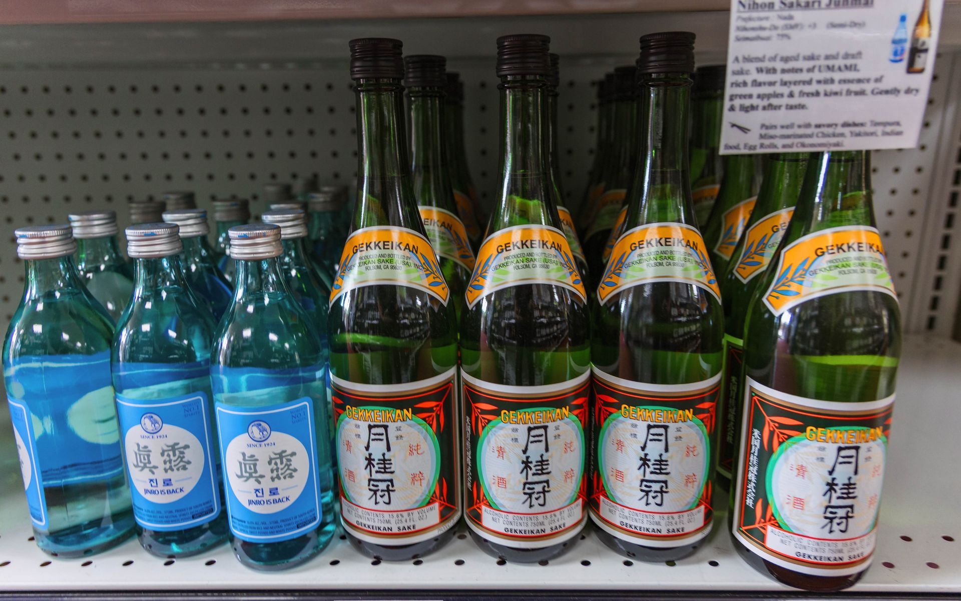 Bottles of sake in a store, some green and some blue, on a shelf.