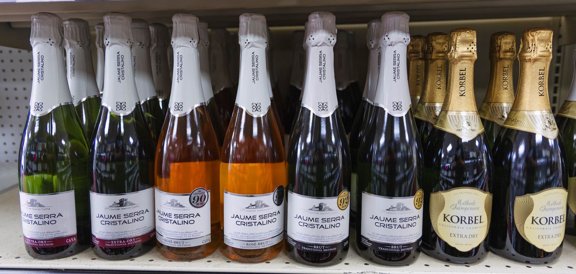 Bottles of champagne on a shelf, with some green, rosé, and gold bottles visible.