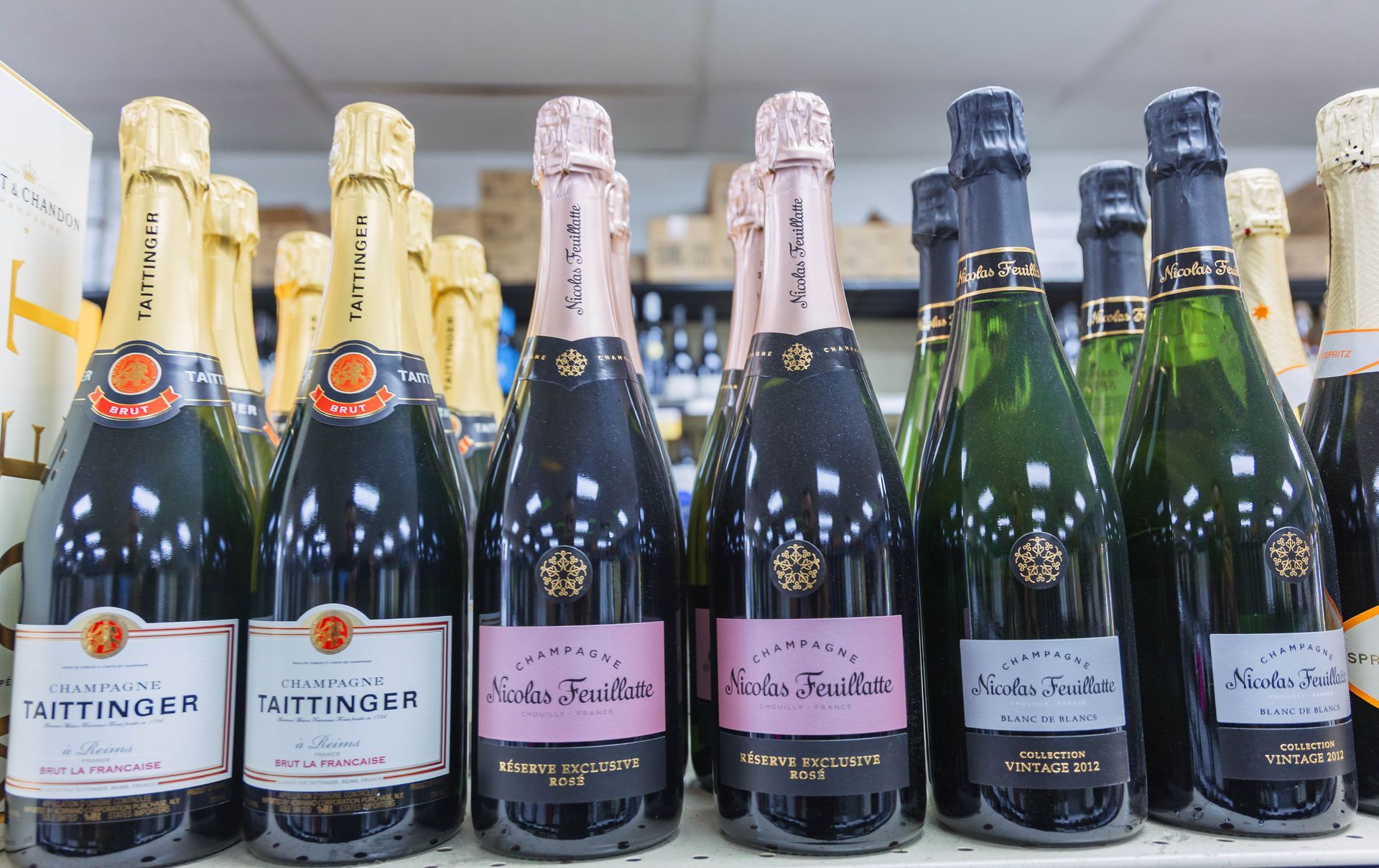 Bottles of sparkling wine in a liquor store. Several bottles have gold or pink foil, and pink or black labels.
