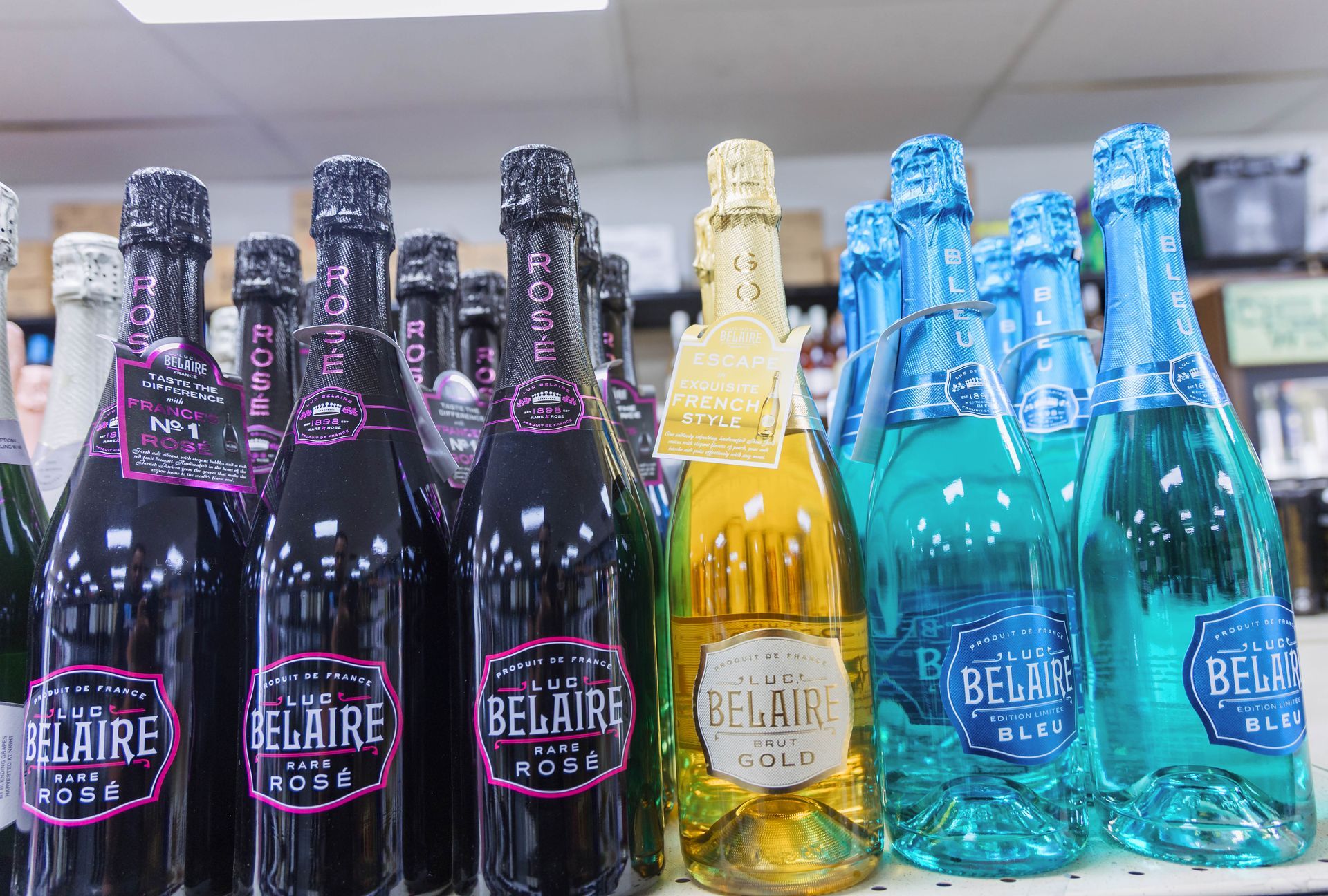 Bottles of Belaire sparkling wine in various colors on a shelf, including pink, gold, and blue.