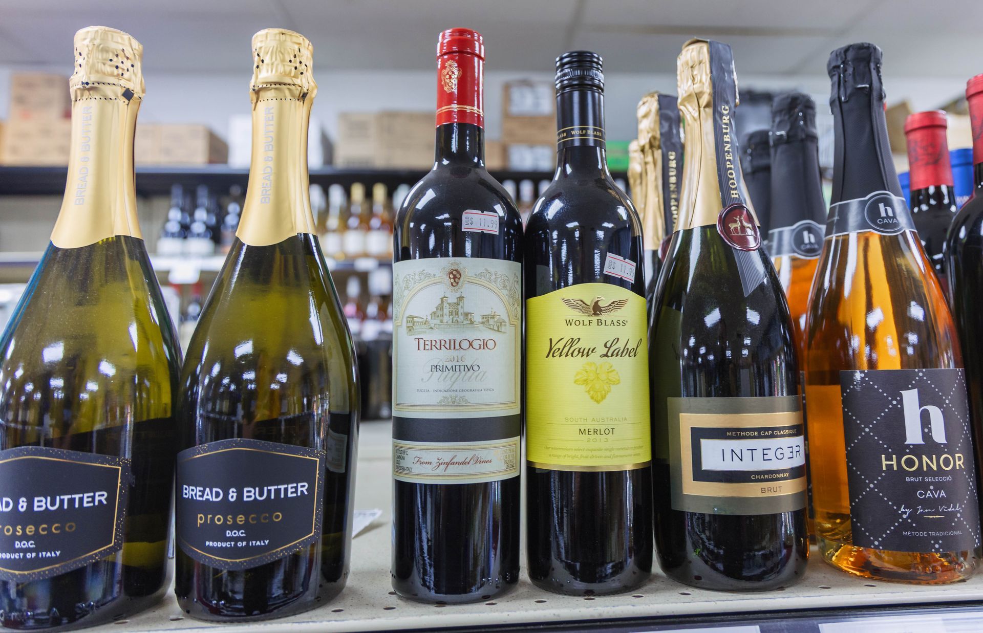 Wine bottles on a shelf, including sparkling, red, and white, in a store setting.