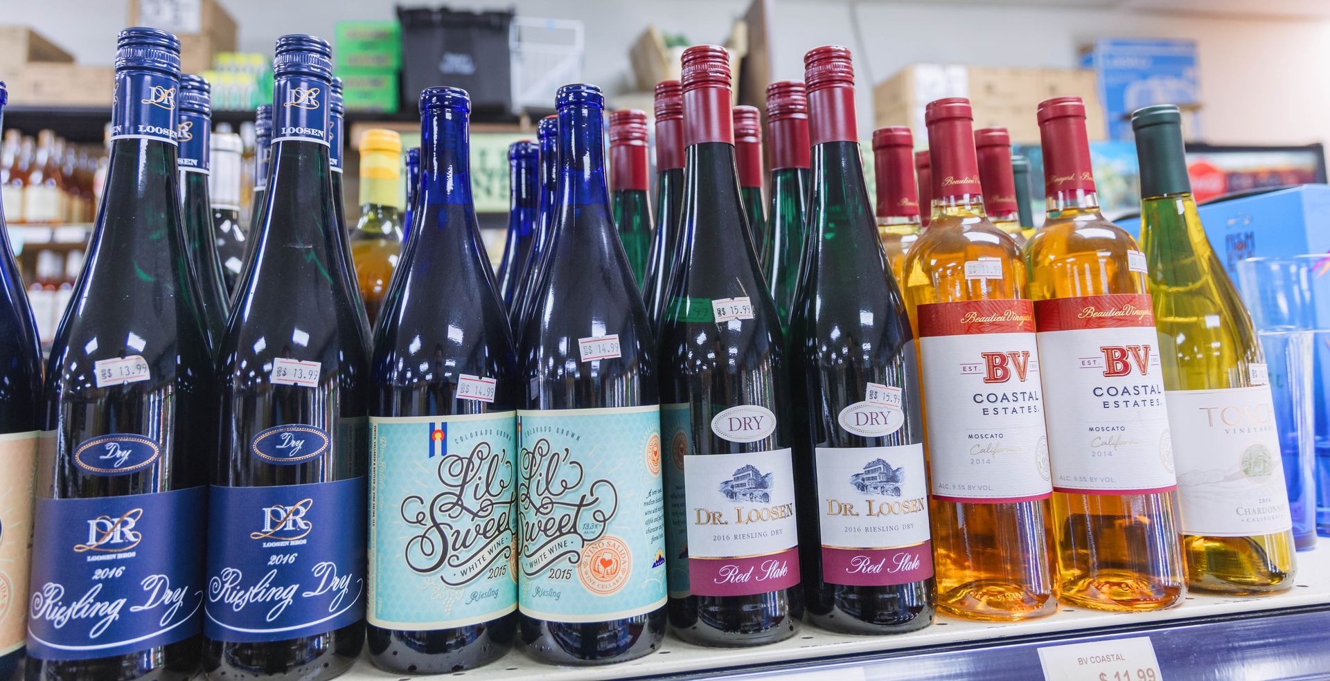 Bottles of wine on a store shelf, various colors, labels visible.