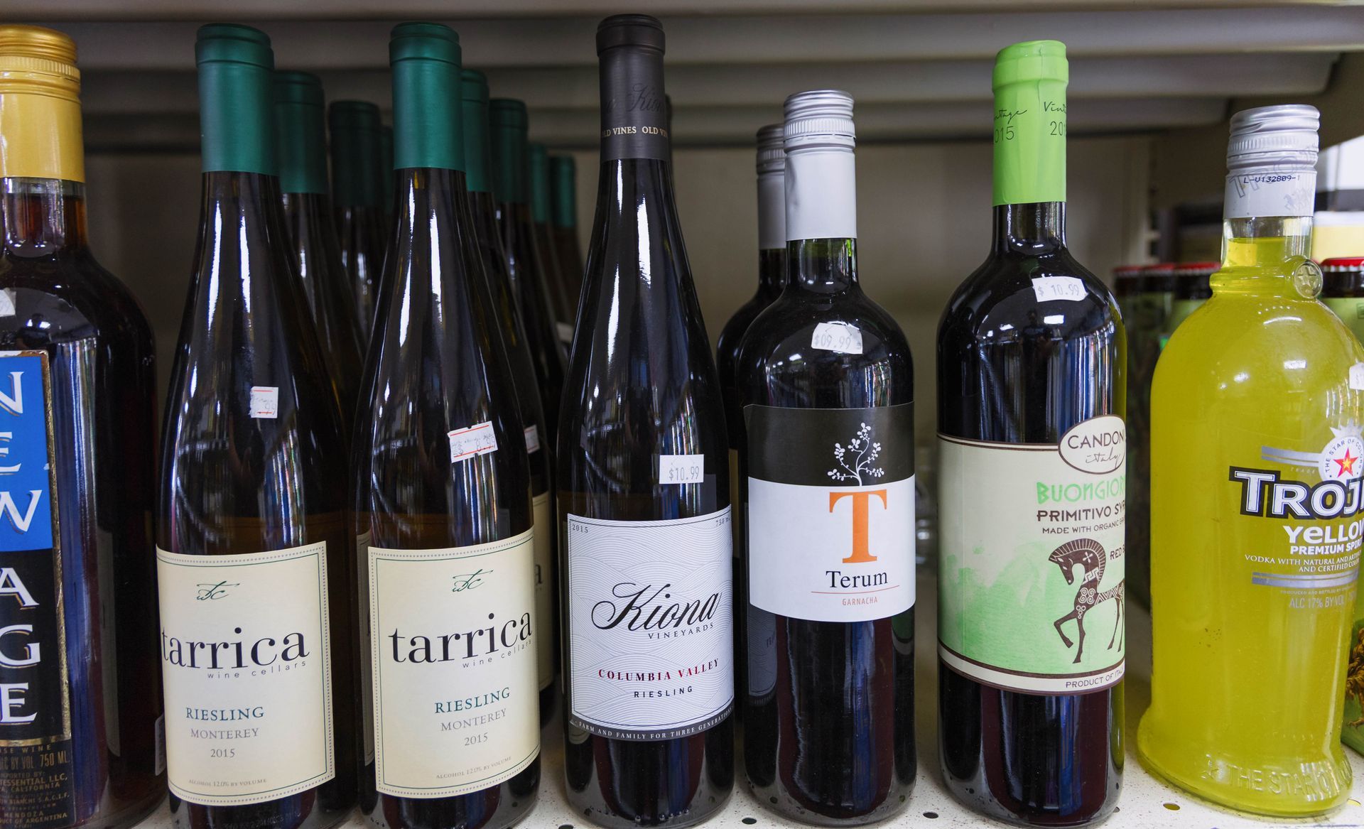Wine bottles on a shelf, some with white labels, some with green and one yellow.