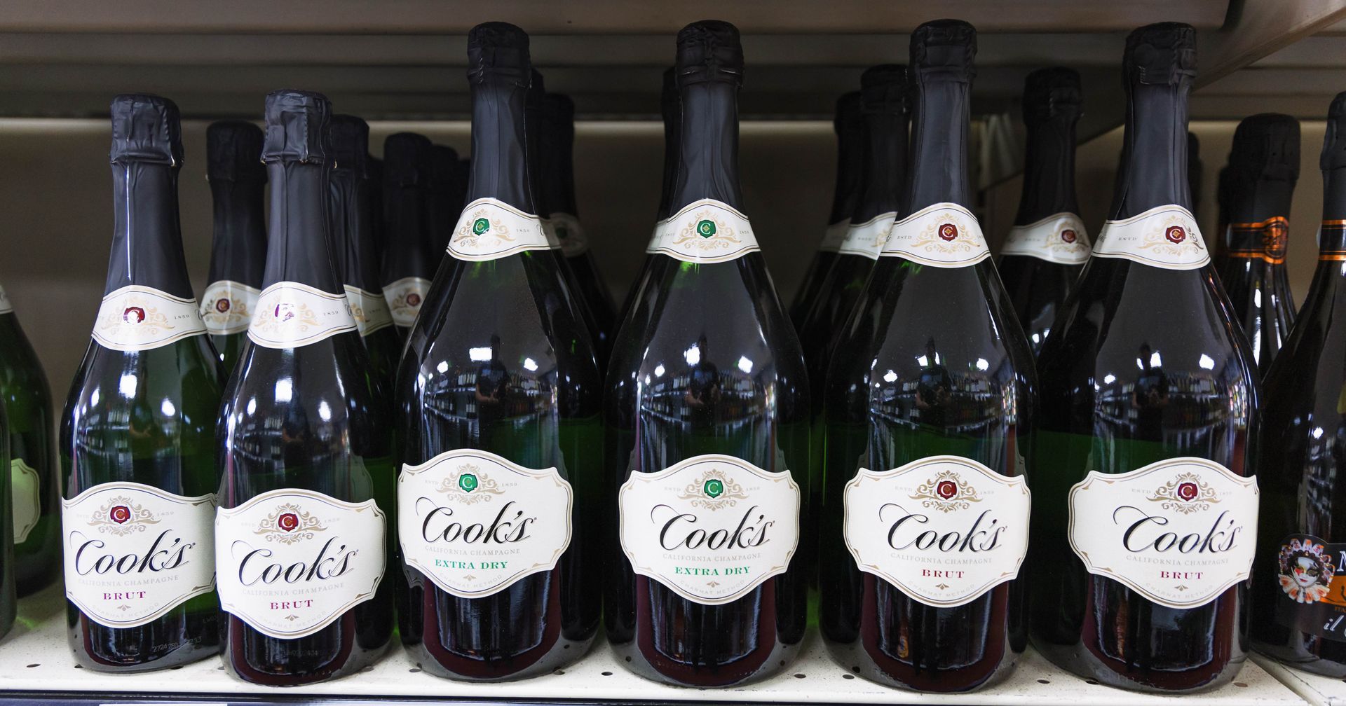 Bottles of Cook's sparkling wine with black caps and white labels displayed on a shelf.