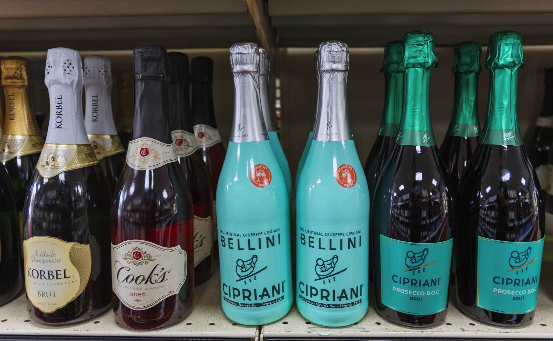 Bottles of sparkling wine on a shelf, with various labels and colors, including blue and green.