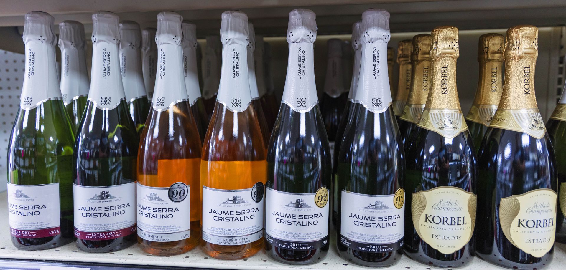 Bottles of sparkling wine on a shelf; various colors and brands.