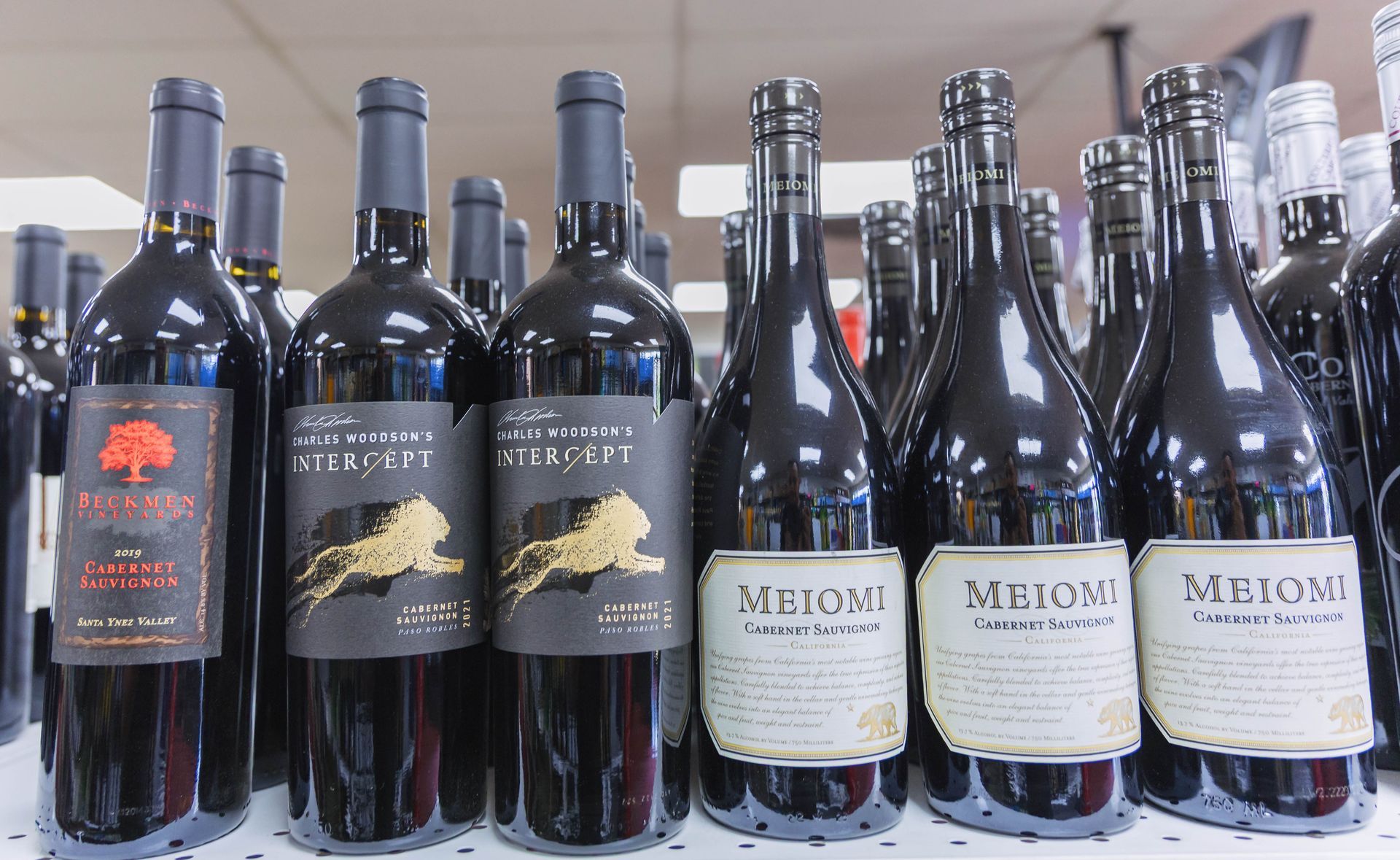 Bottles of red wine on a shelf, with black and white labels.