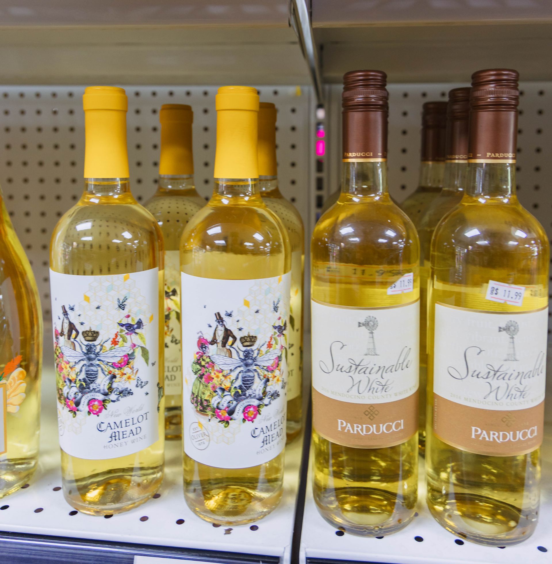 Bottles of white wine on a shelf with colorful labels and yellow caps.