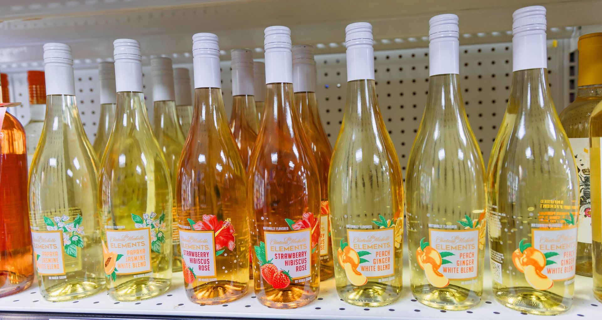 Bottles of wine on a shelf; various colors from light yellow to orange.