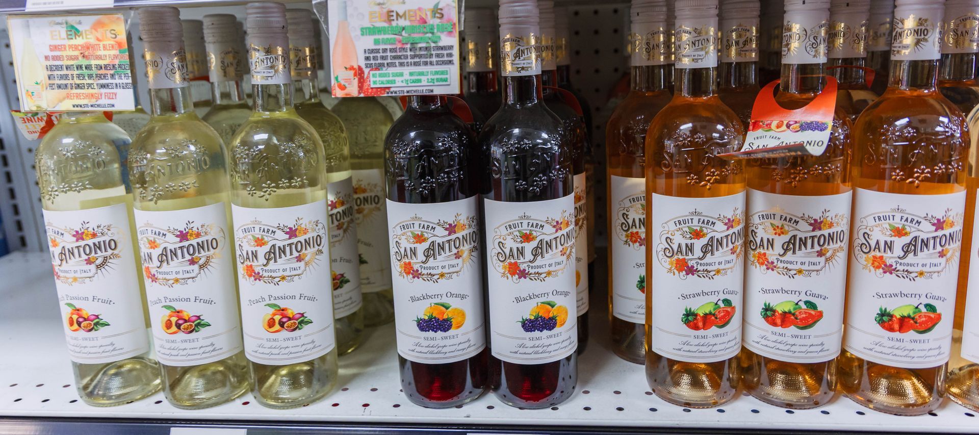 Bottles of wine displayed on shelves. Some white, some red, and some orange-tinted with colorful labels.