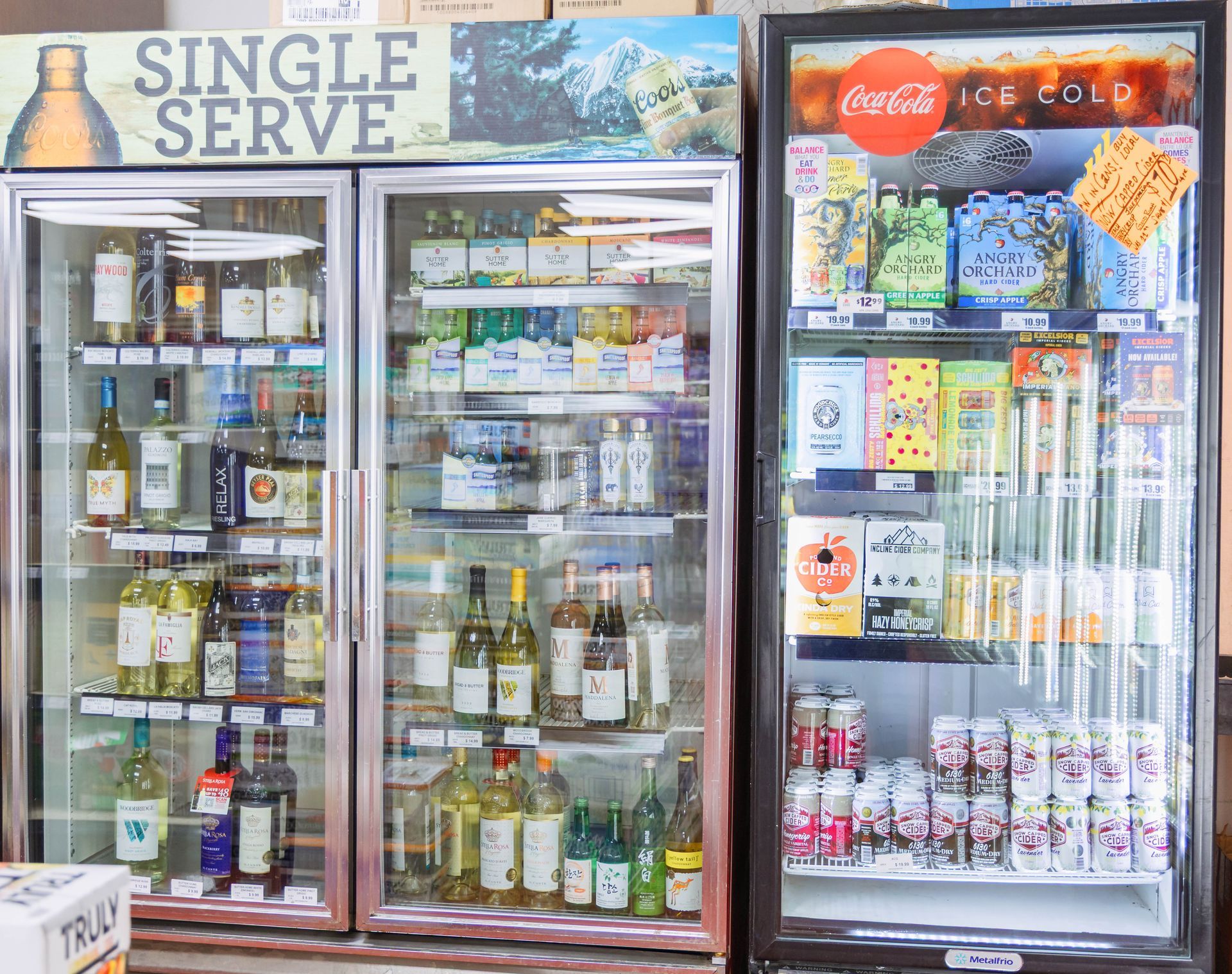 Refrigerated coolers displaying single-serve beverages including alcohol, soda, and snacks in a store.