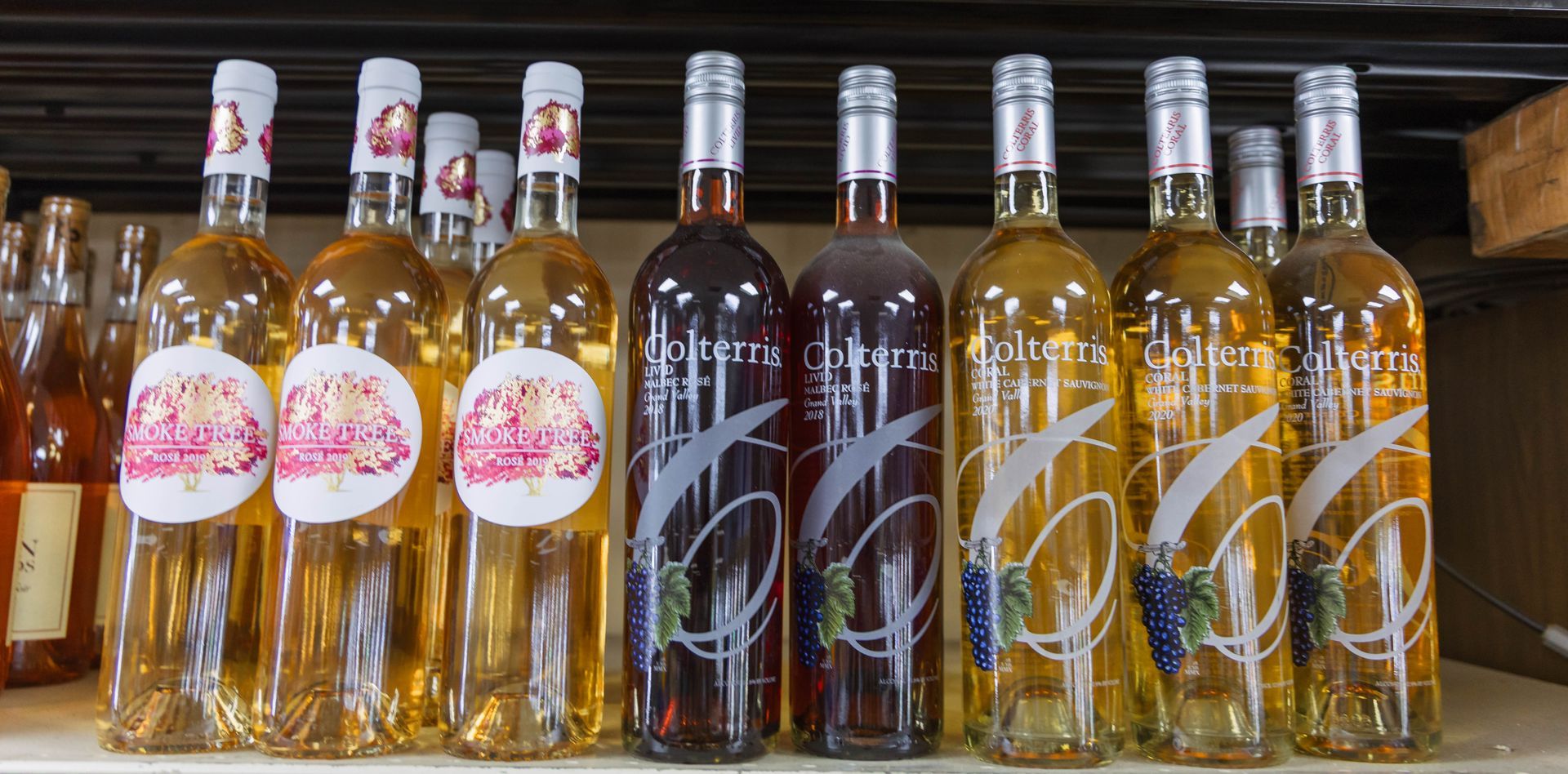 Bottles of wine on a shelf, varying in color from red to yellow, with ornate labels and silver tops.