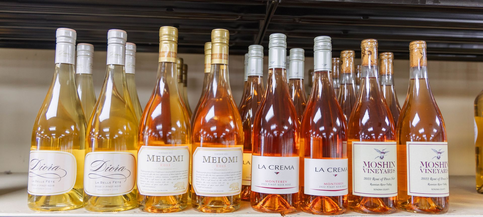 Bottles of rosé and white wine on a shelf.