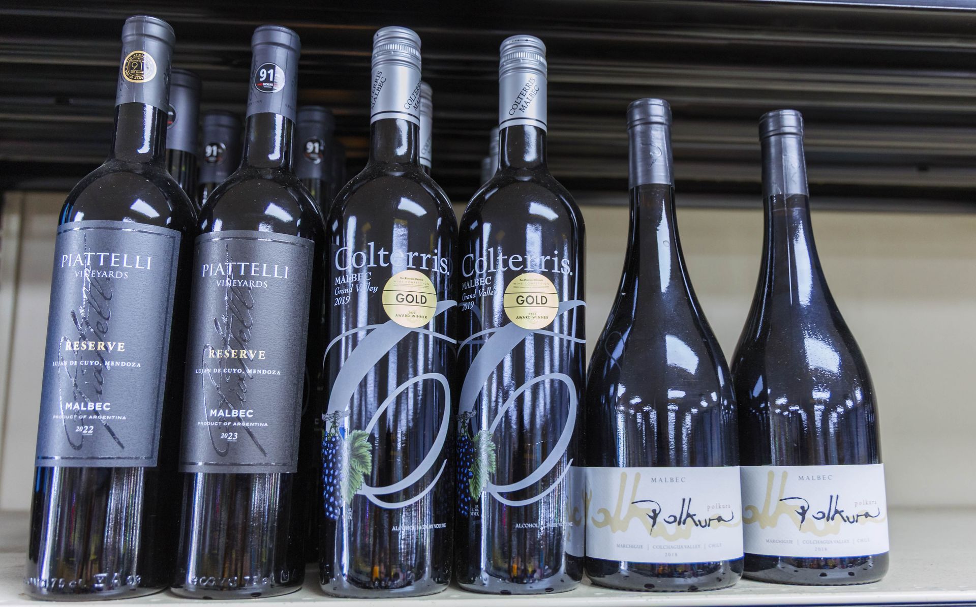 Bottles of wine on a shelf, with various labels in black, silver, and white.