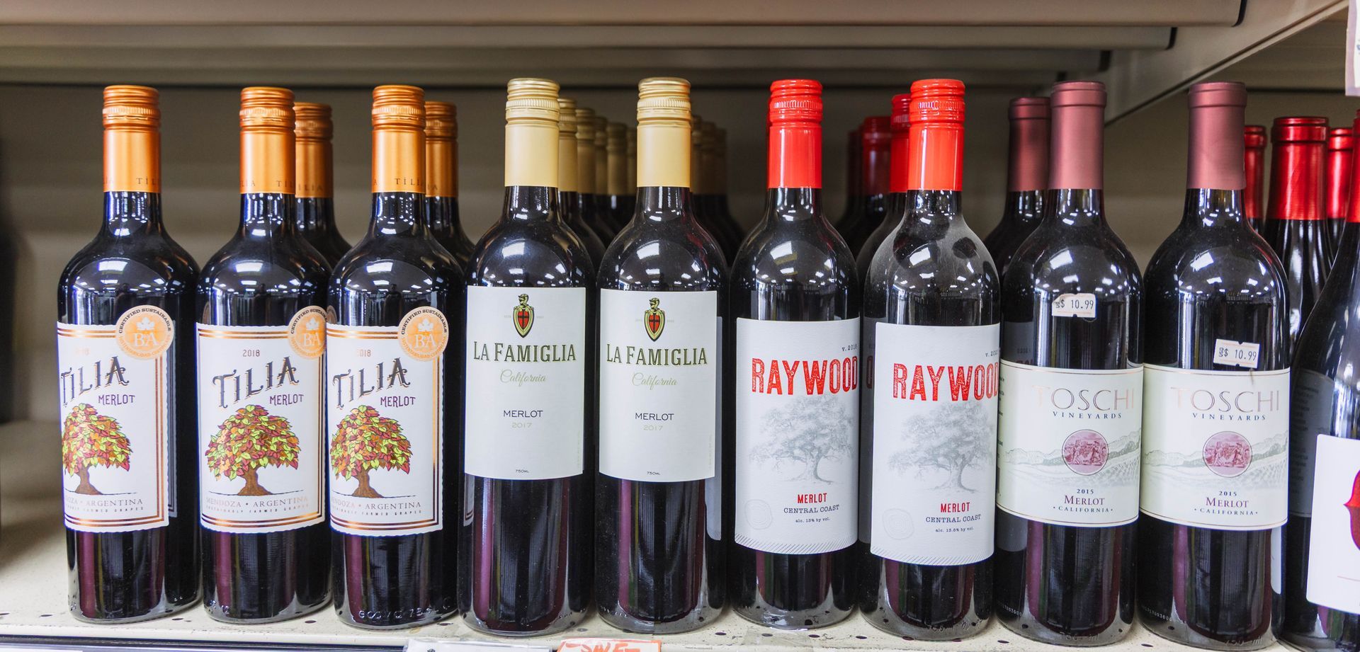 Row of red wine bottles on a store shelf; different labels, colors, and styles.