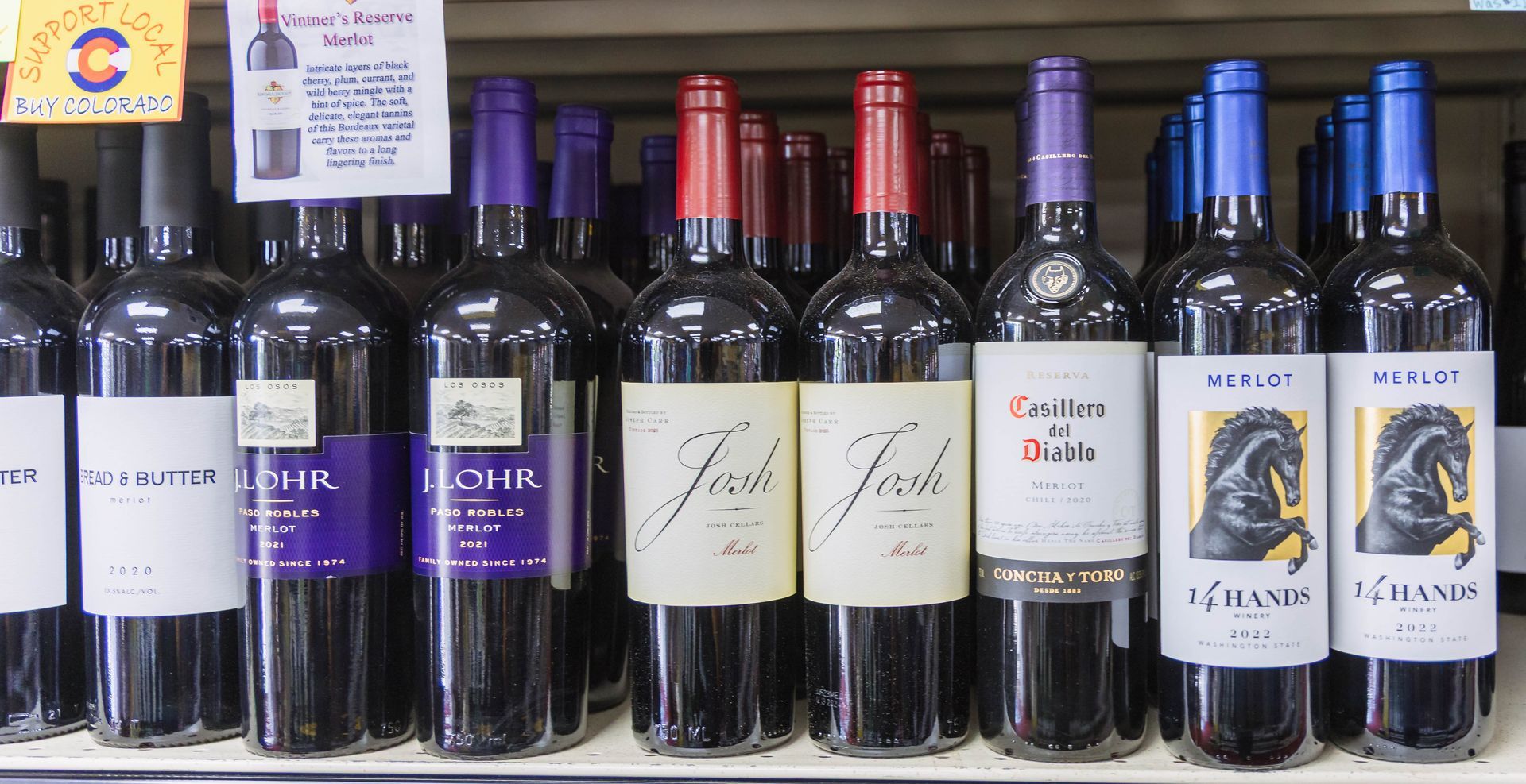 Wine bottles on a shelf with various colored caps.