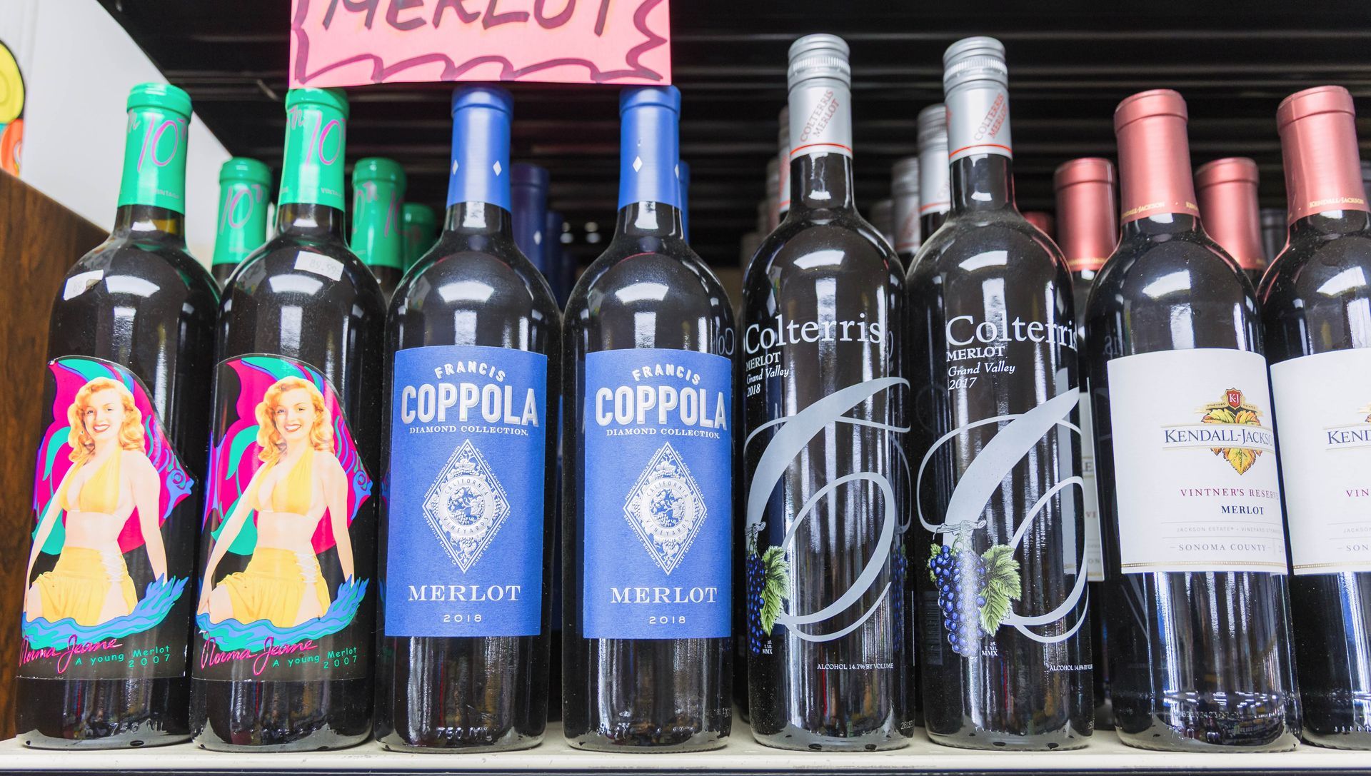 Bottles of Merlot wine on a shelf, various labels in shades of blue, green, and pink.