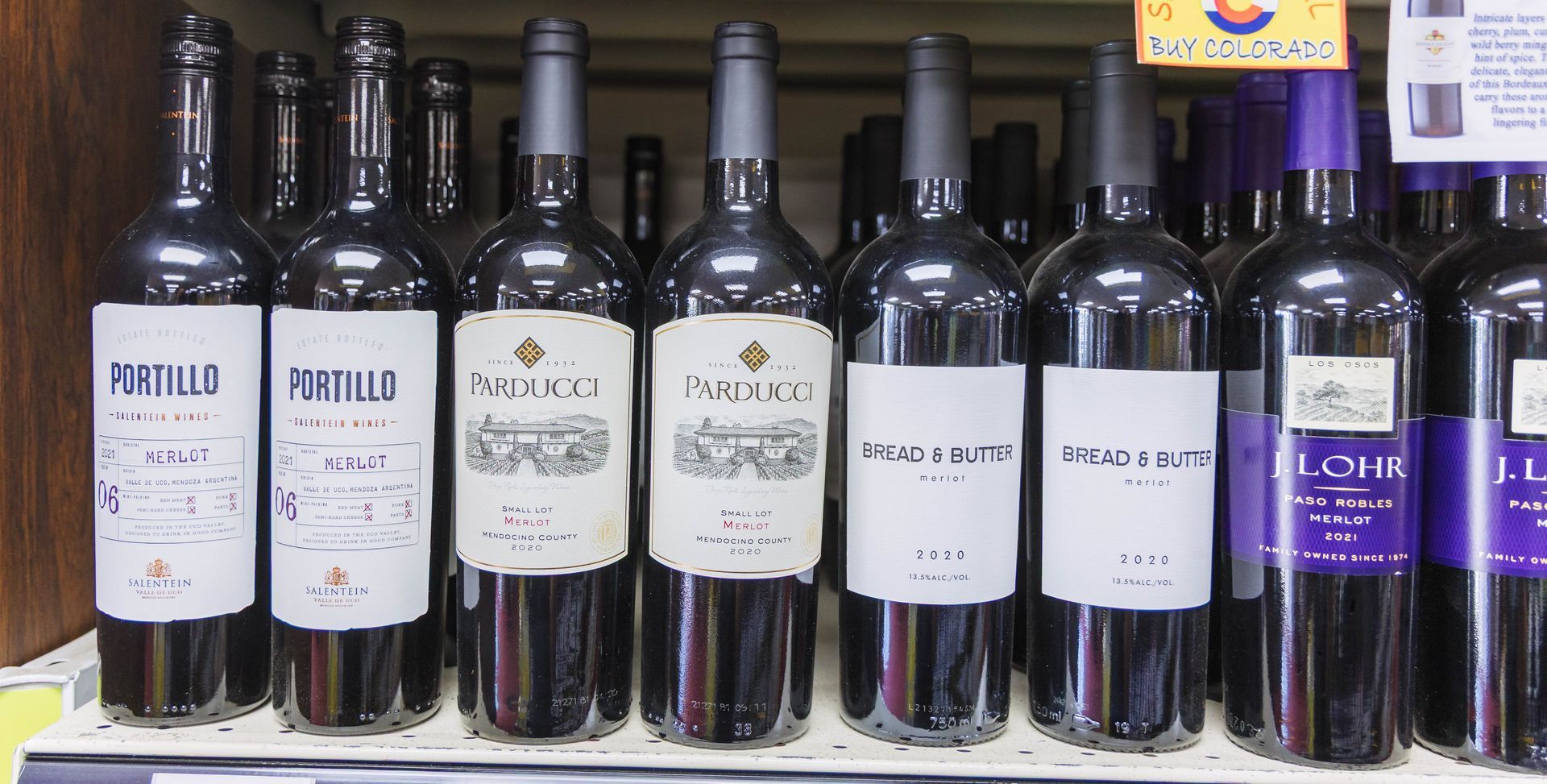 Rows of red wine bottles on a shelf, with labels and dark glass.