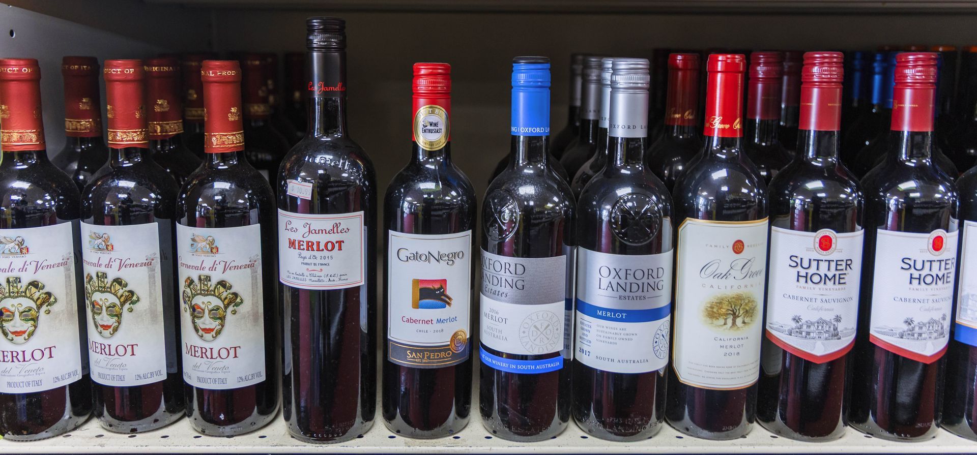Bottles of red wine lined up on a shelf in a store. Different labels and caps.