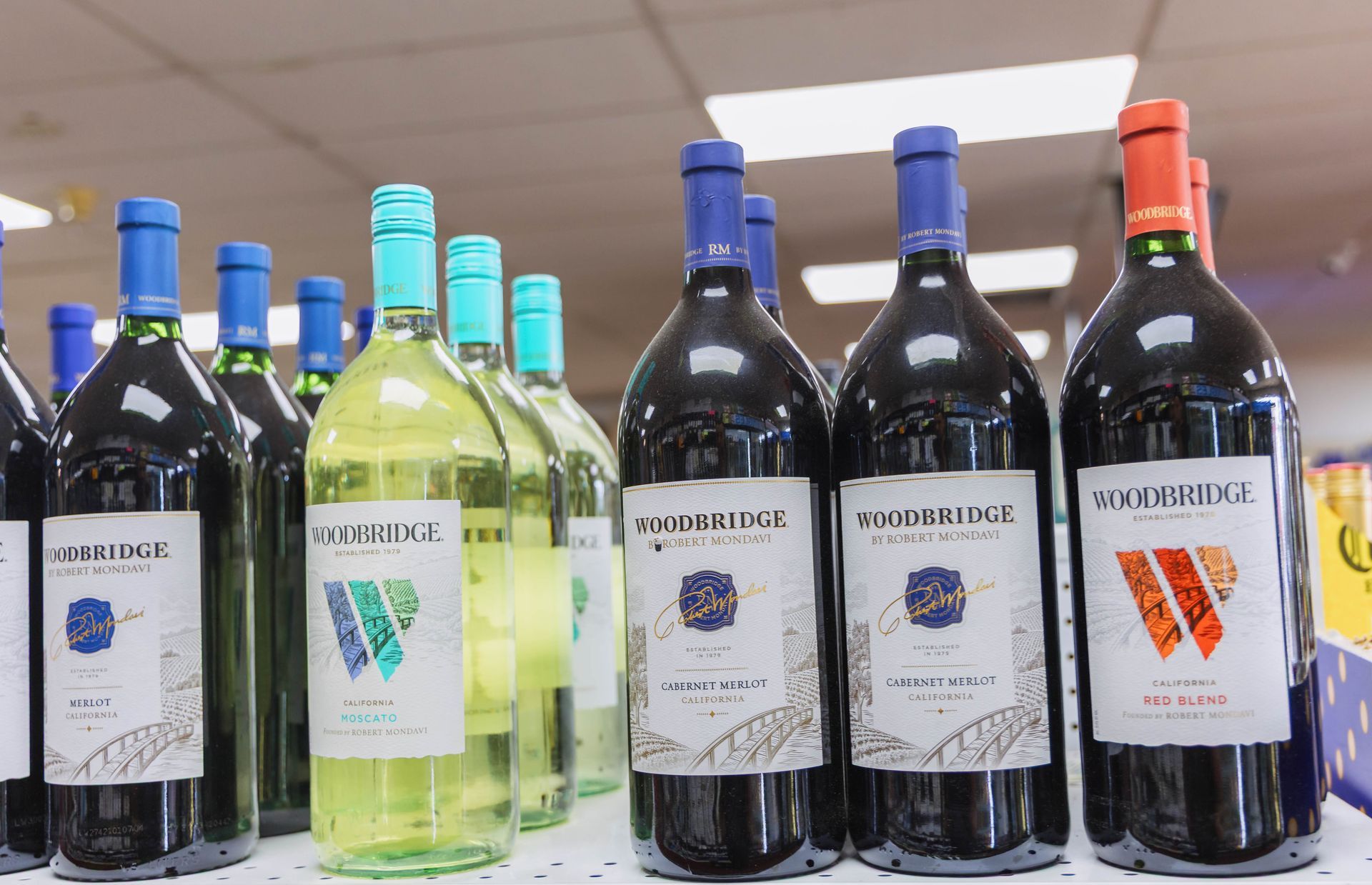 Bottles of Woodbridge wine on a store shelf, some red, some white, various colored bottle tops.