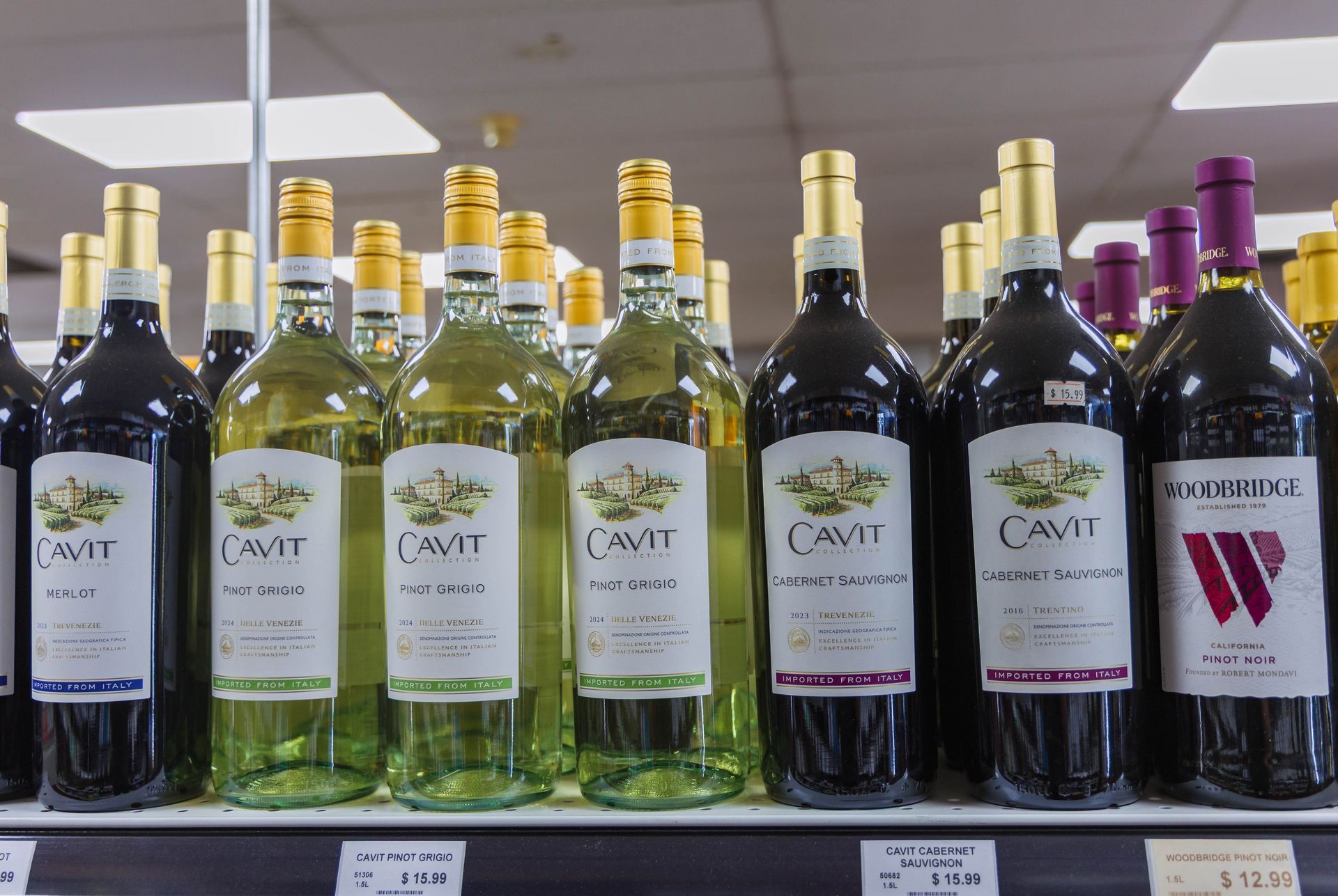 Bottles of Cavit and Woodbridge wine on a shelf, white and red, lit by overhead lights.