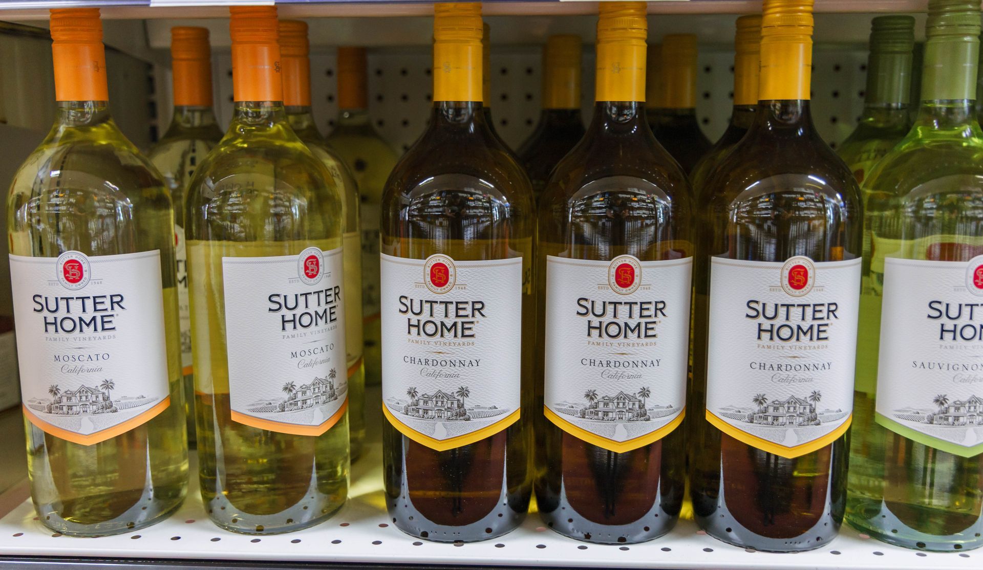 Bottles of Sutter Home white wine on a shelf, orange and yellow labels and caps.