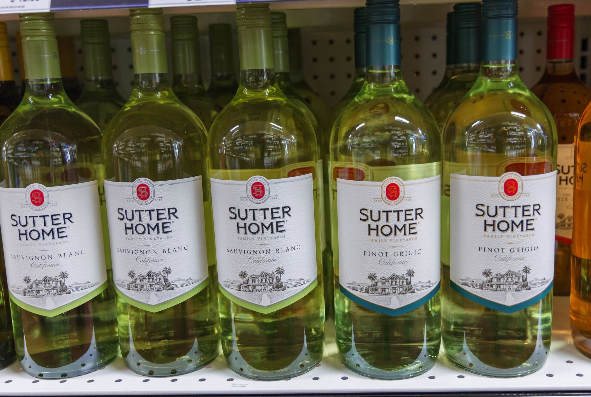 Row of Sutter Home wine bottles on a shelf; green bottles with white labels and a green-tinted liquid.