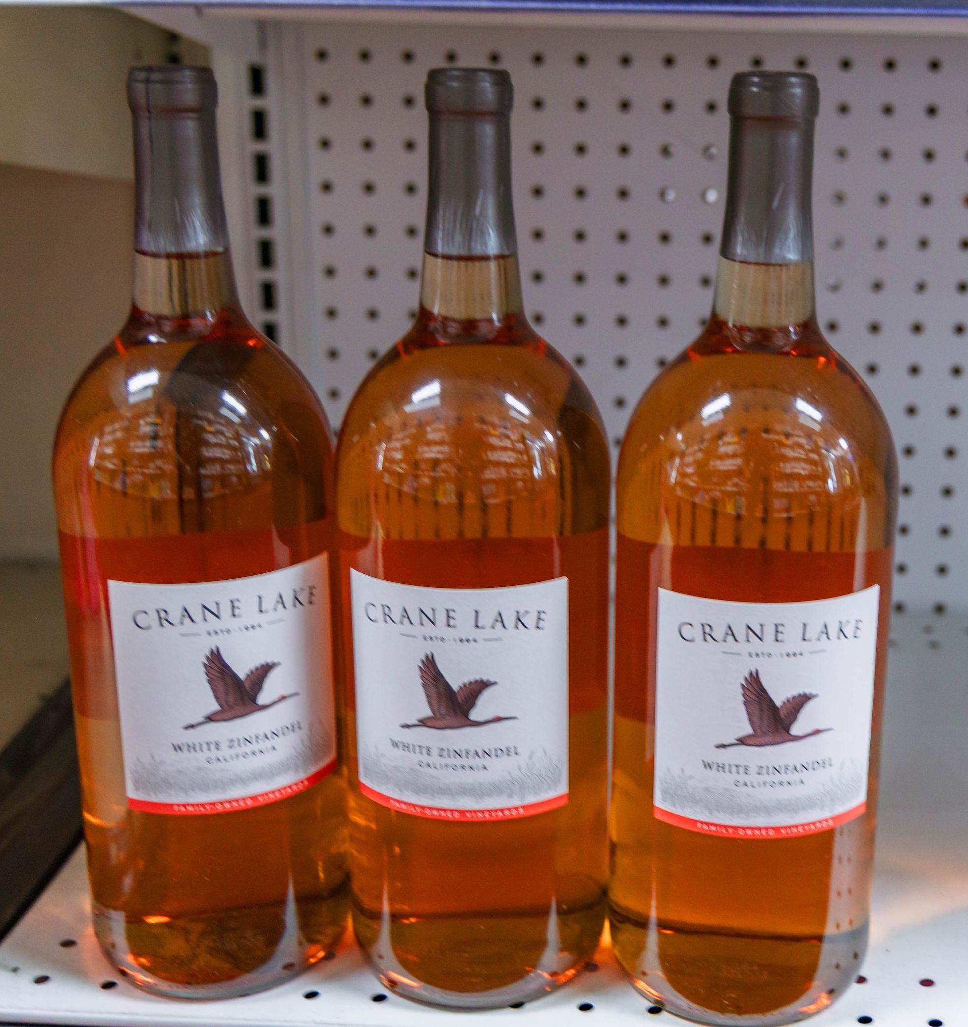 Three bottles of Crane Lake rosé wine on a shelf. The bottles have a label with a flying bird image.
