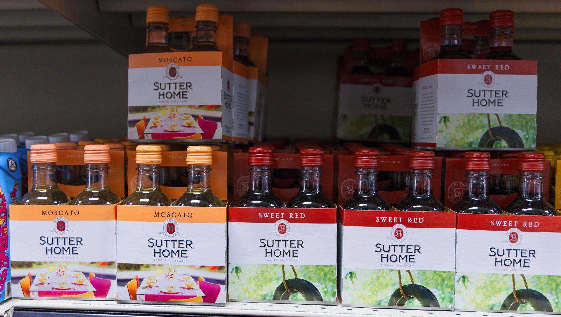 Sutter Home wine bottles in various flavors, orange and red boxes, on store shelf.