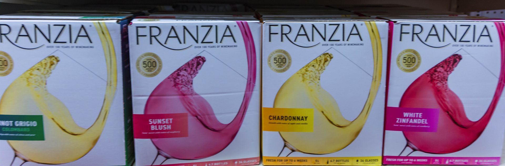 Four Franzia wine boxes with different colors and varieties on a shelf.