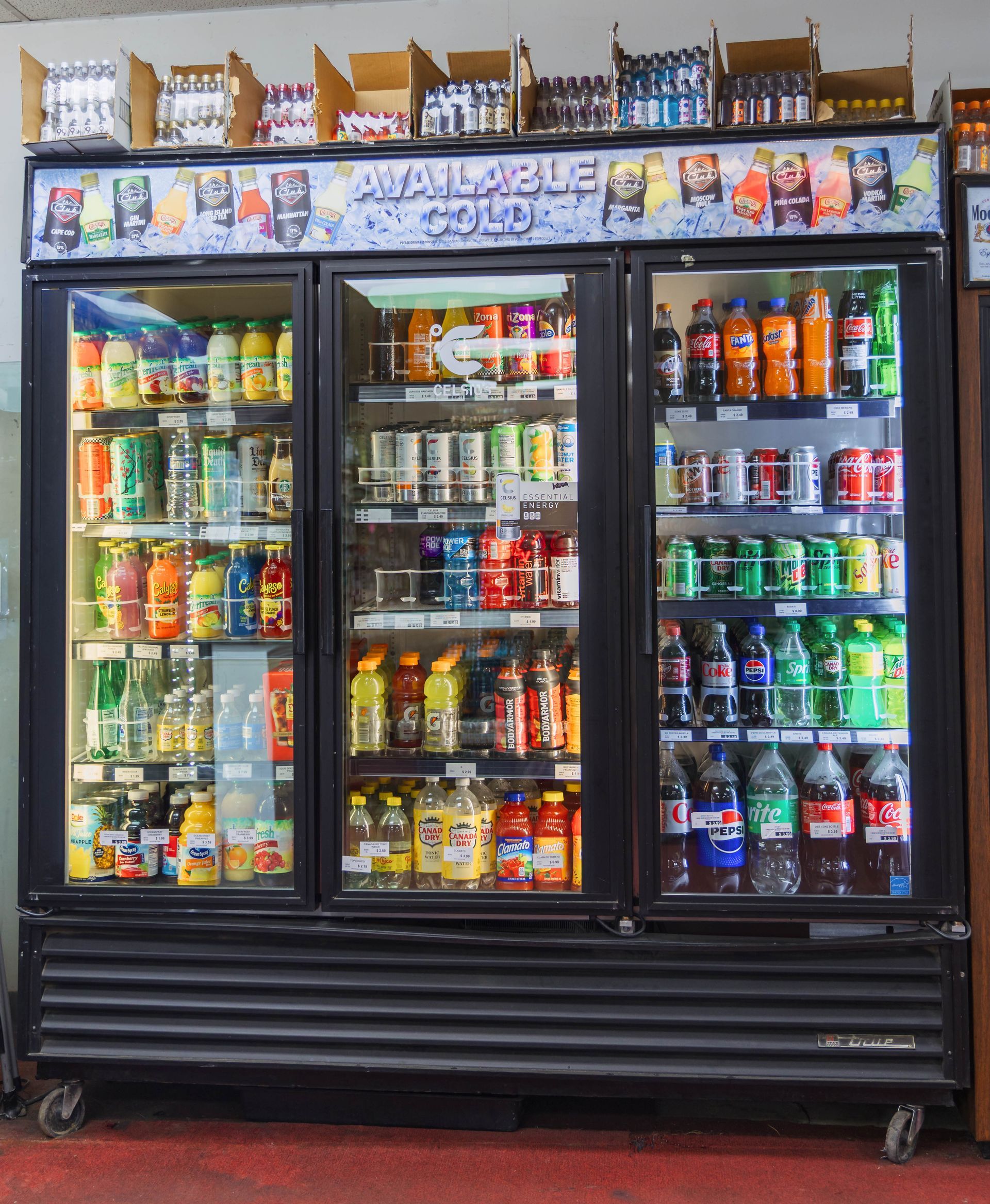 A triple-door beverage cooler filled with colorful drinks. Cans and bottles, brightly lit.
