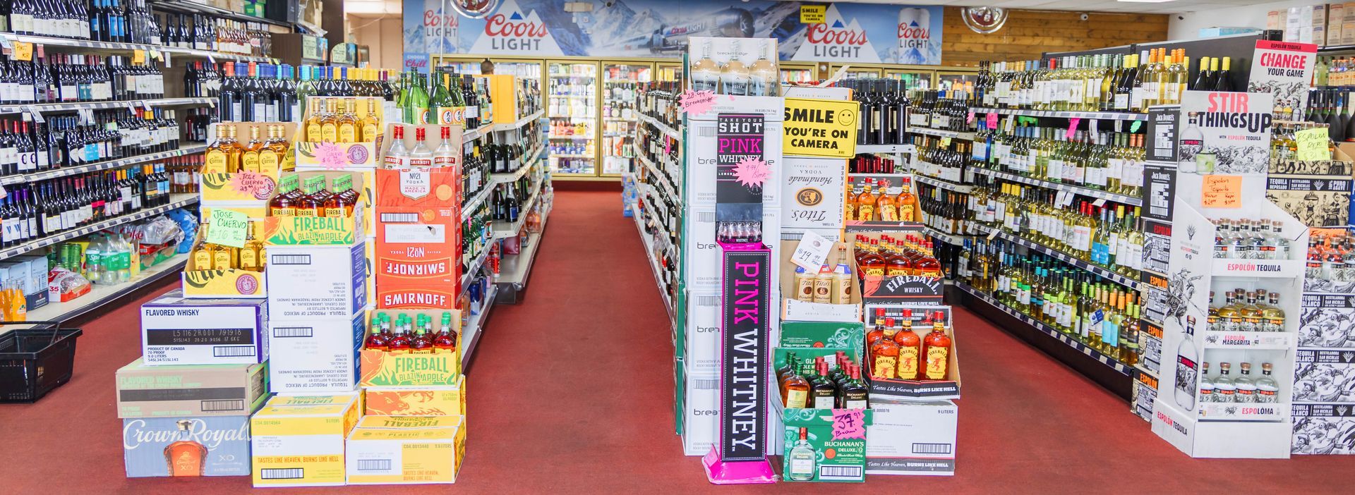 A liquor store interior with aisles of alcohol and product displays on the red floor.