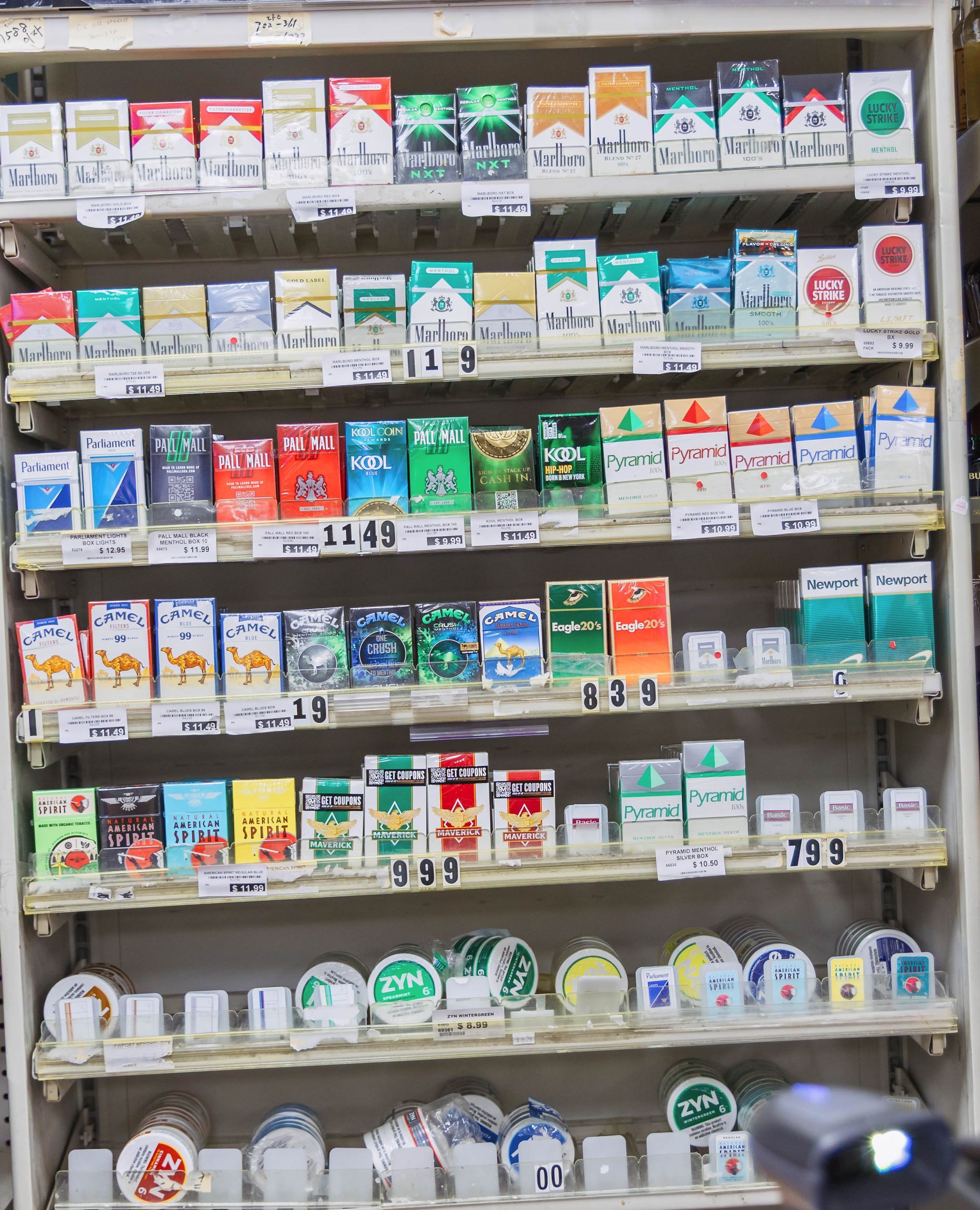 Shelves stocked with numerous cigarette packs in various colors and brands, likely in a convenience store.