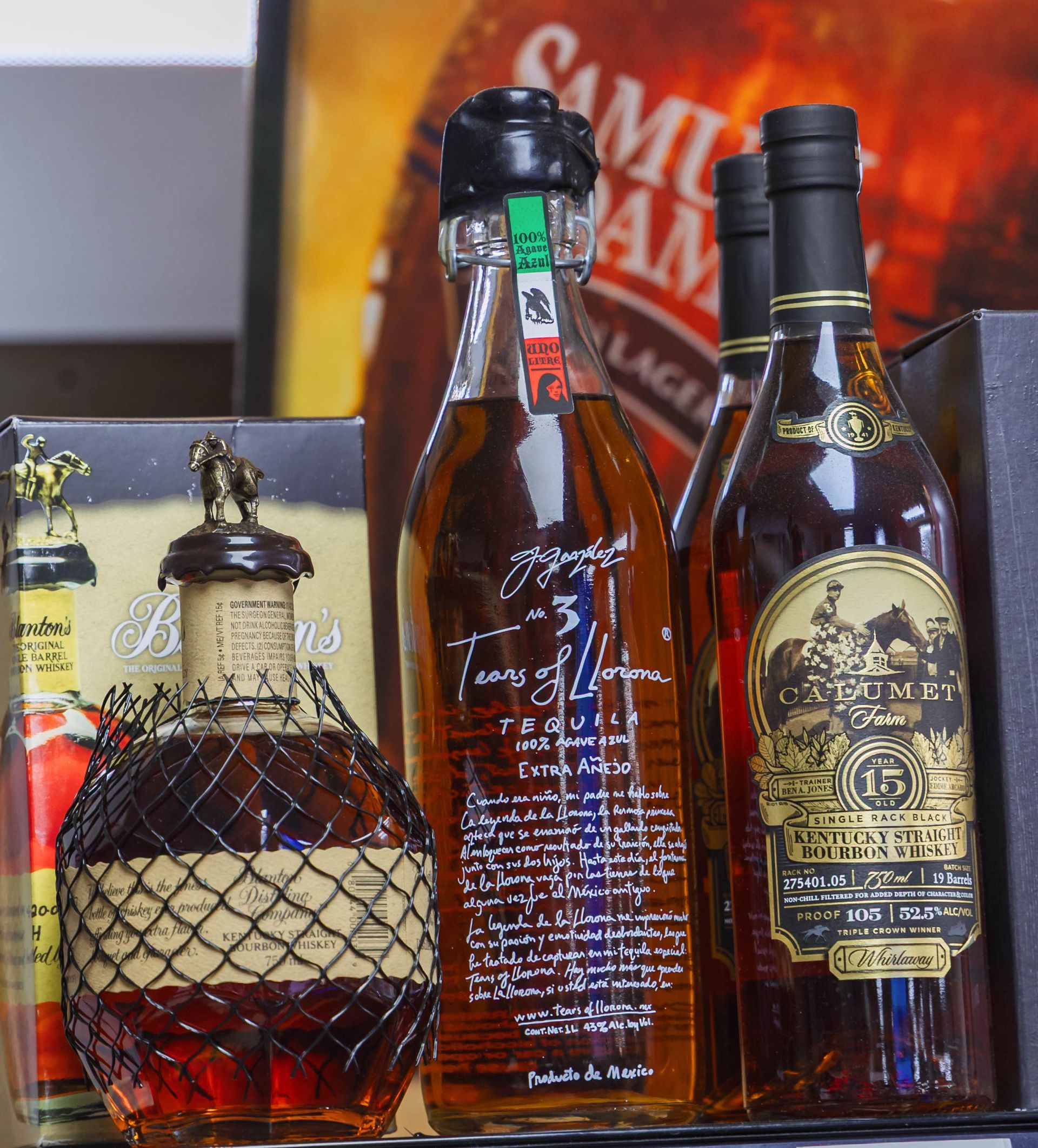 Bottles of liquor on a shelf, including a Blanton's bottle with a bronze topper, in a dimly lit setting.